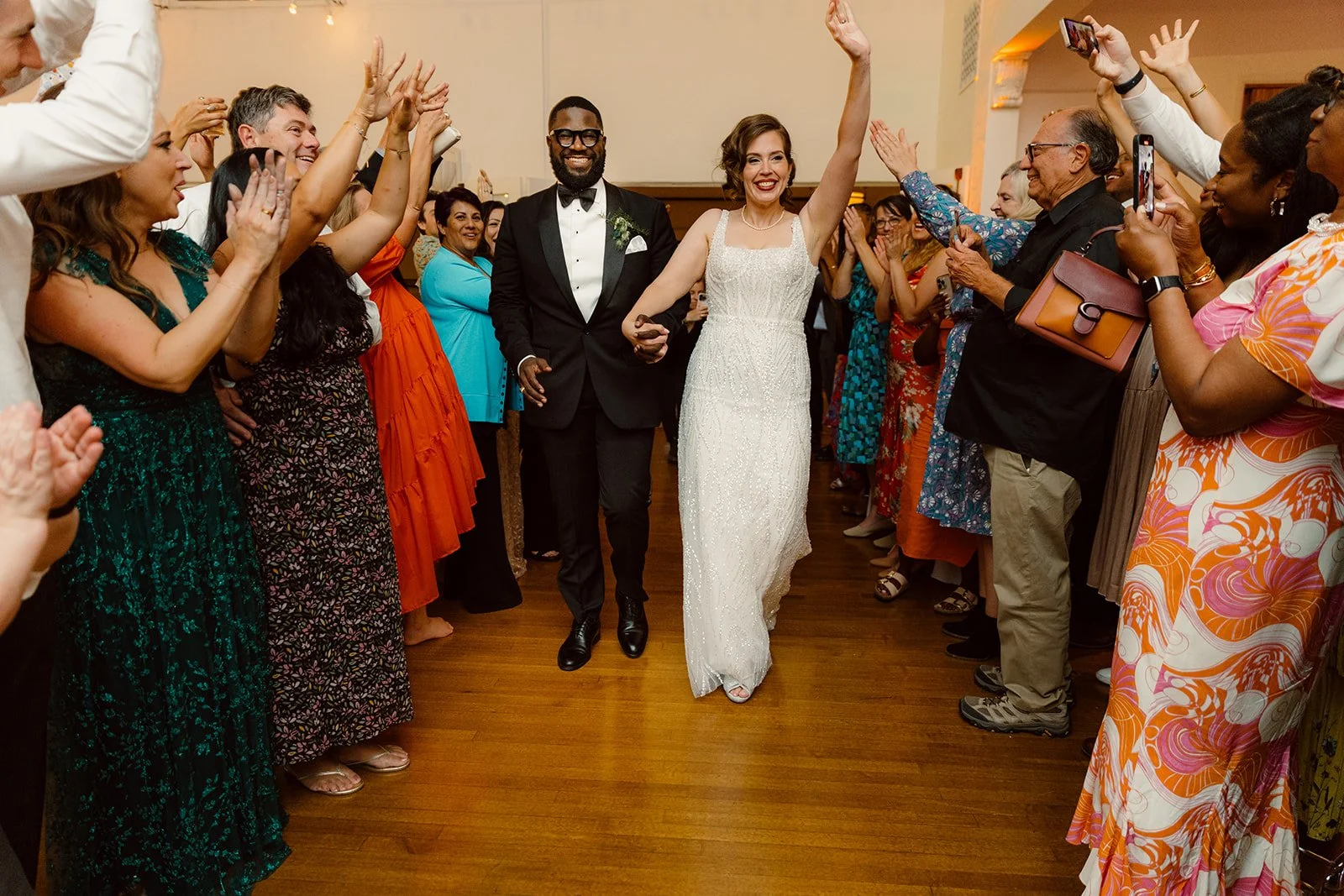 Couple holds hands and waves at their cheering guests on their final wedding exit in San Diego at Thursday Club venue.