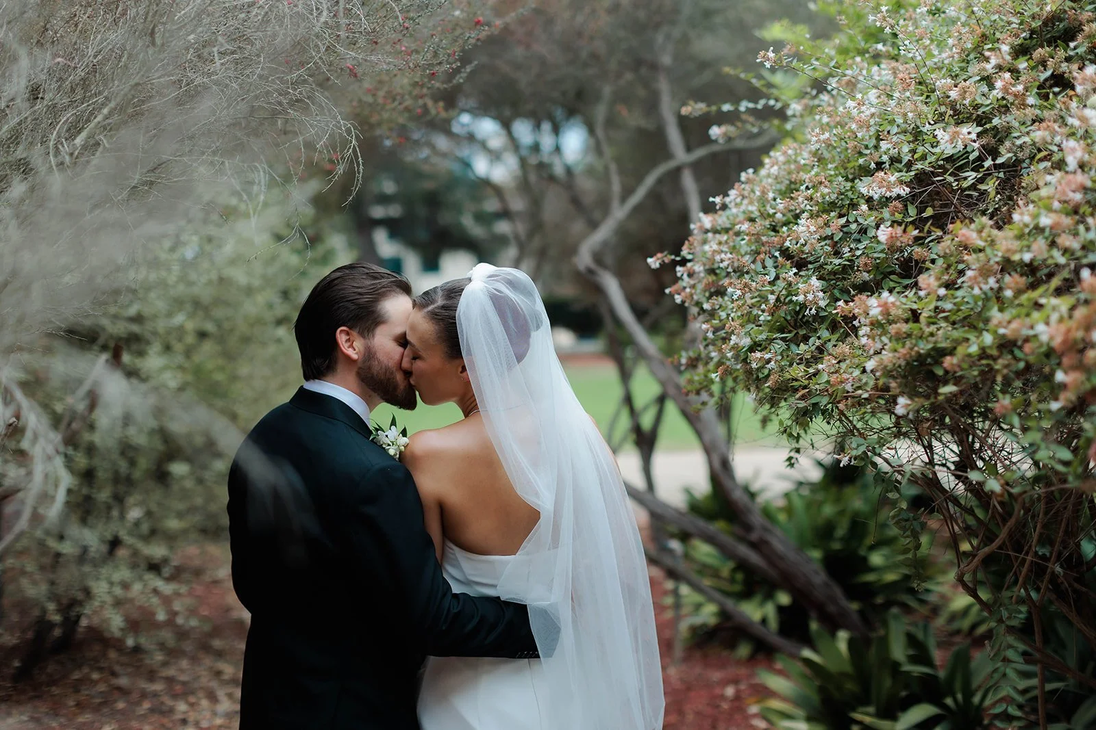 Bride and groom kiss in the lush walkways of the Marston House in Balboa Park.
