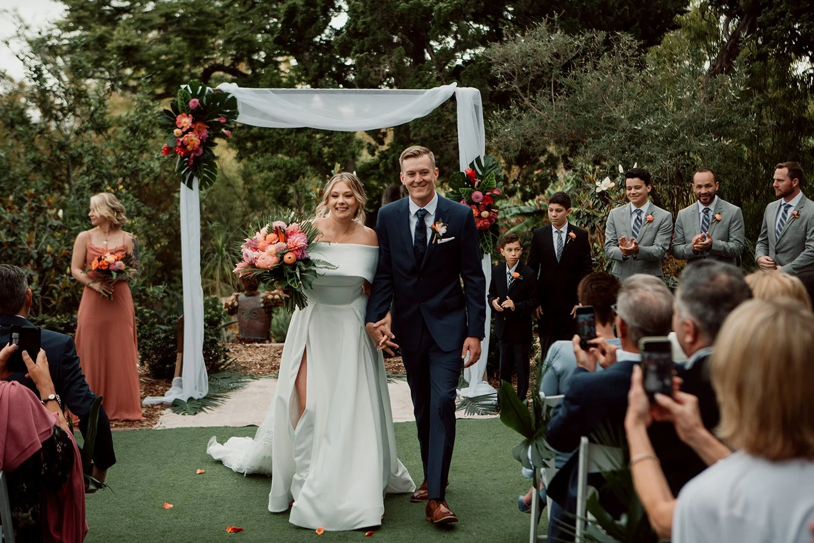 San Diego Botanic Garden wedding ceremony exit shows bride and groom walking out after first kiss while guests clap and look on.