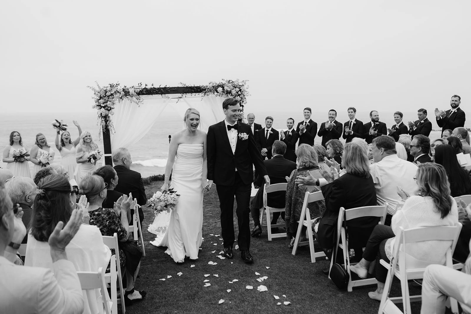 Bride and groom exit their ceremony at the Wedding Bowl while guests cheer and clap.