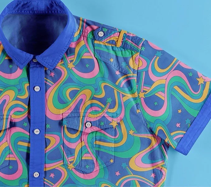 Colorful short-sleeve button-up shirt with rainbow swirl and star pattern, blue collar and trim.