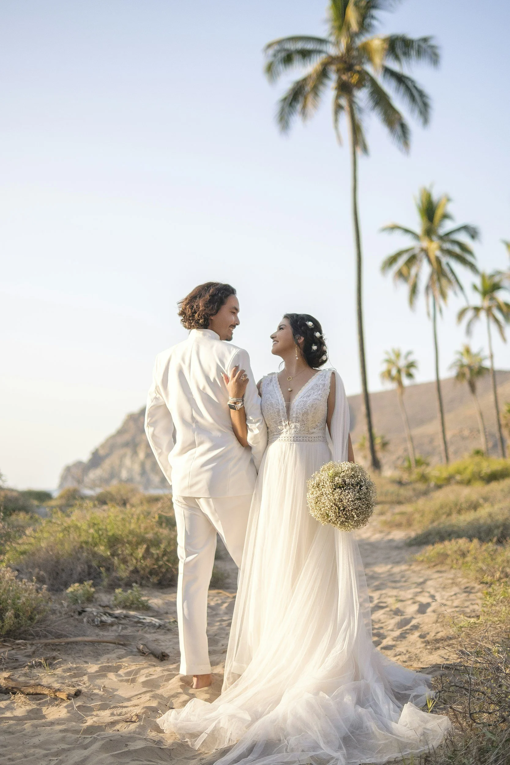 Couple in wedding attire standing beneath palm trees at a tropical destination.