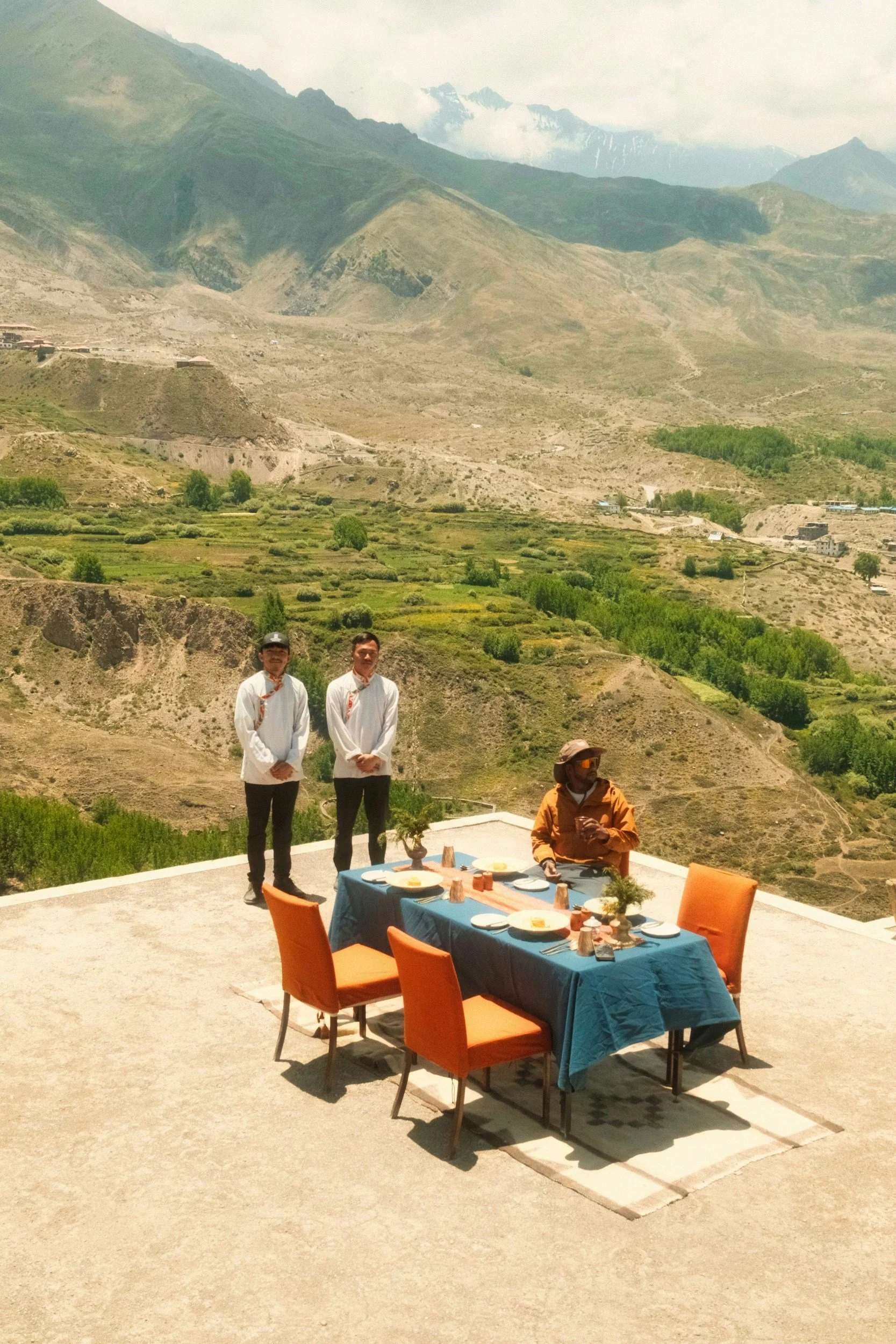 Small group gathered around an outdoor dining table overlooking a mountain landscape.