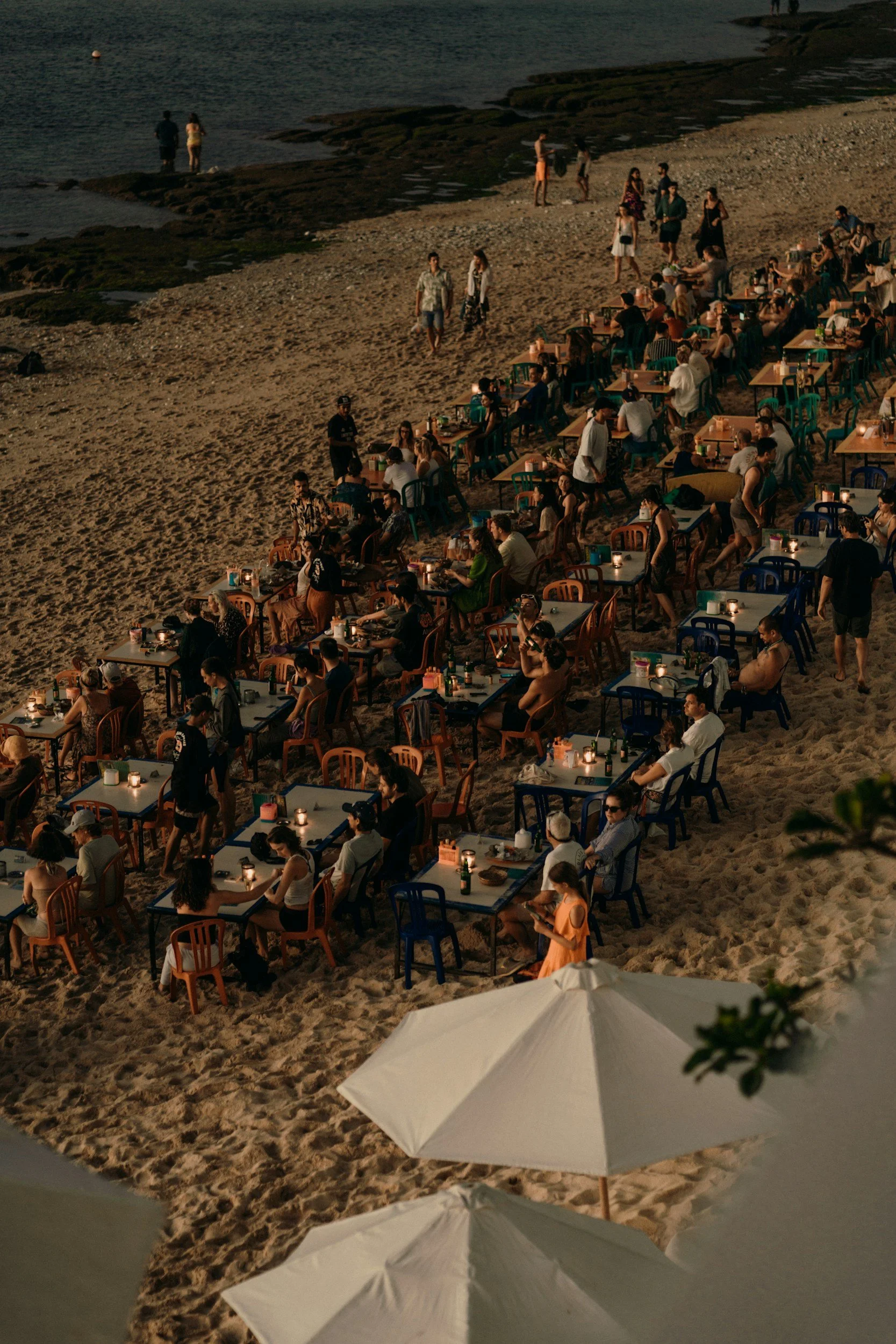 Guests enjoying an outdoor group dinner celebration on a beach at dusk.