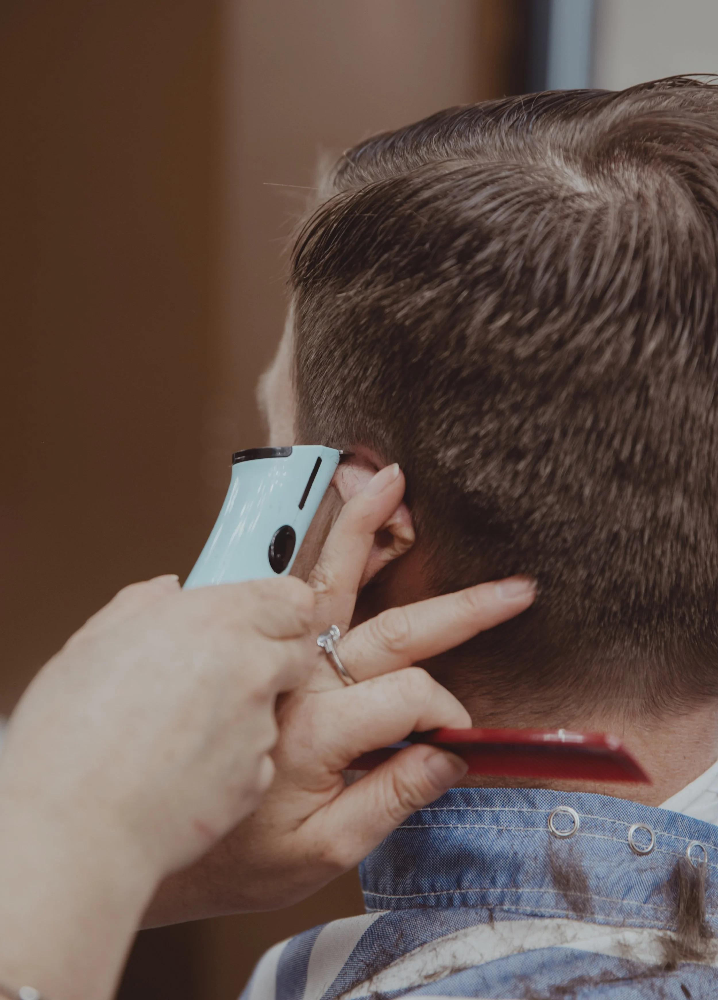 Close-up of a person getting a haircut with electric clippers. A hand holds a blue comb for precision. The setting is a barber shop, conveying a calm, professional tone.