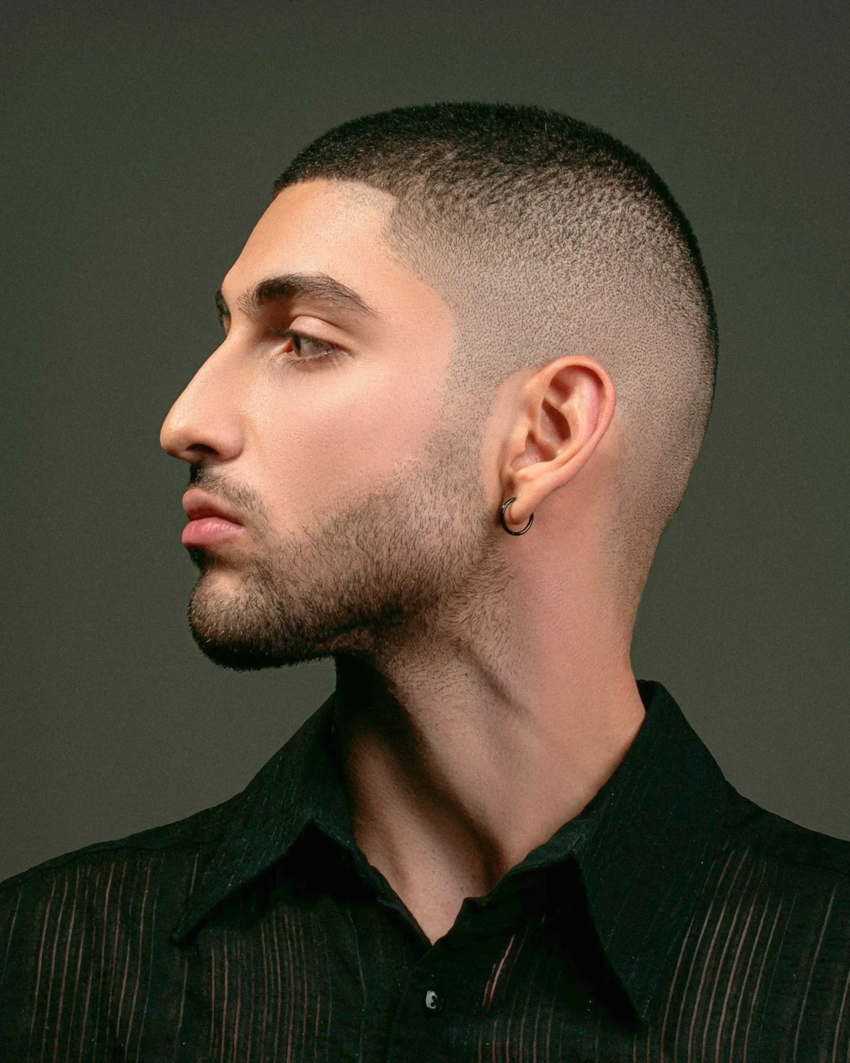 Profile of a man with short hair, wearing a black shirt, looking left. His expression is calm and focused.