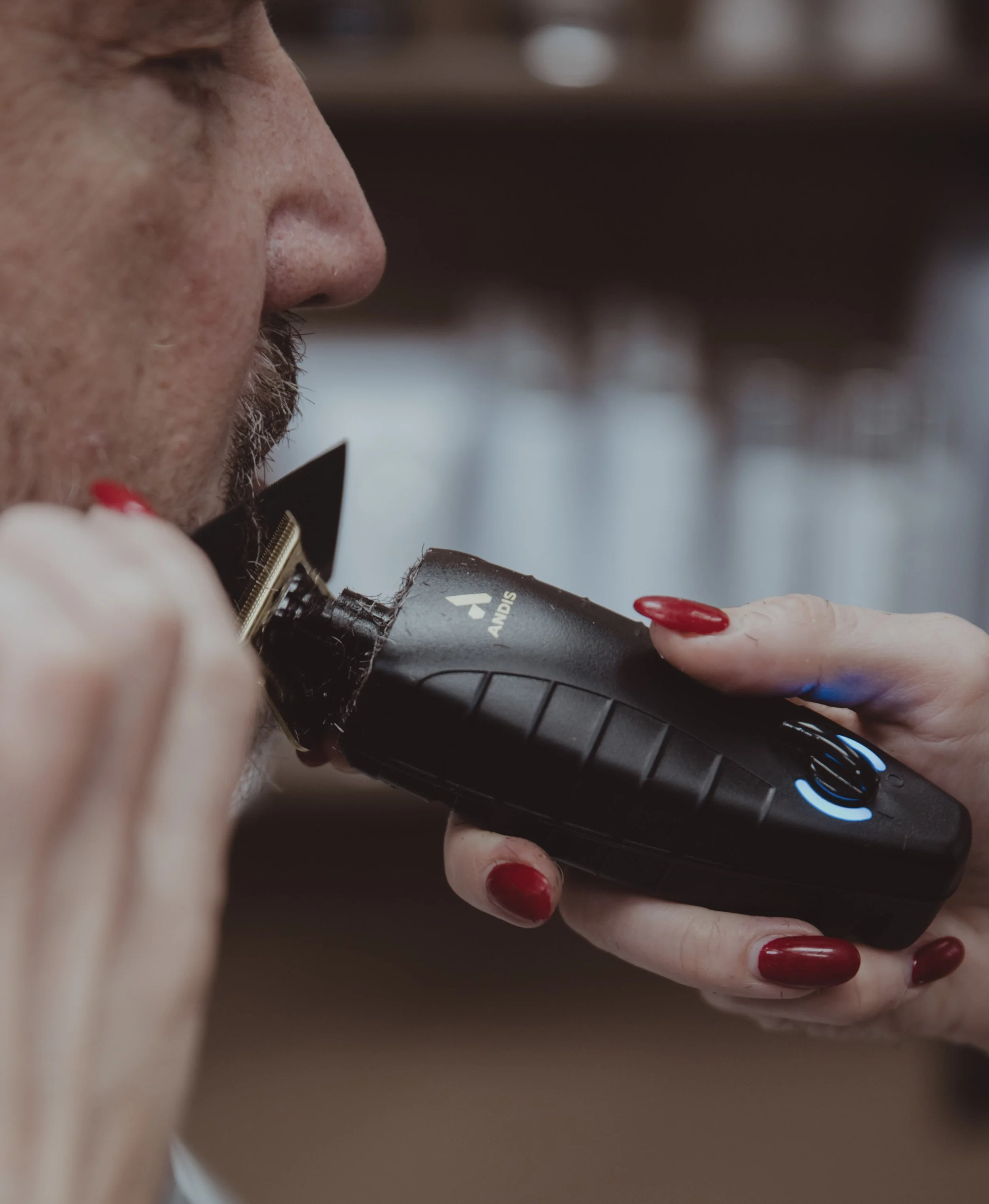 Close-up of a person's face with red-painted nails holding an electronic device labeled Anvis, appearing to be a grooming or grooming-related tool.