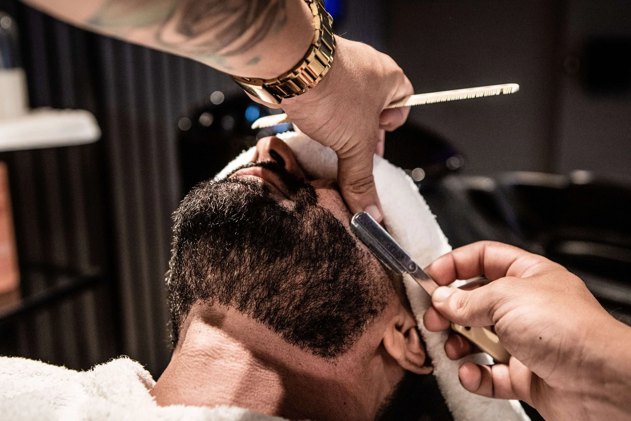 Man receiving a professional shave at a barbershop. A barber uses a straight razor to trim his beard, conveying a sense of precision and care.