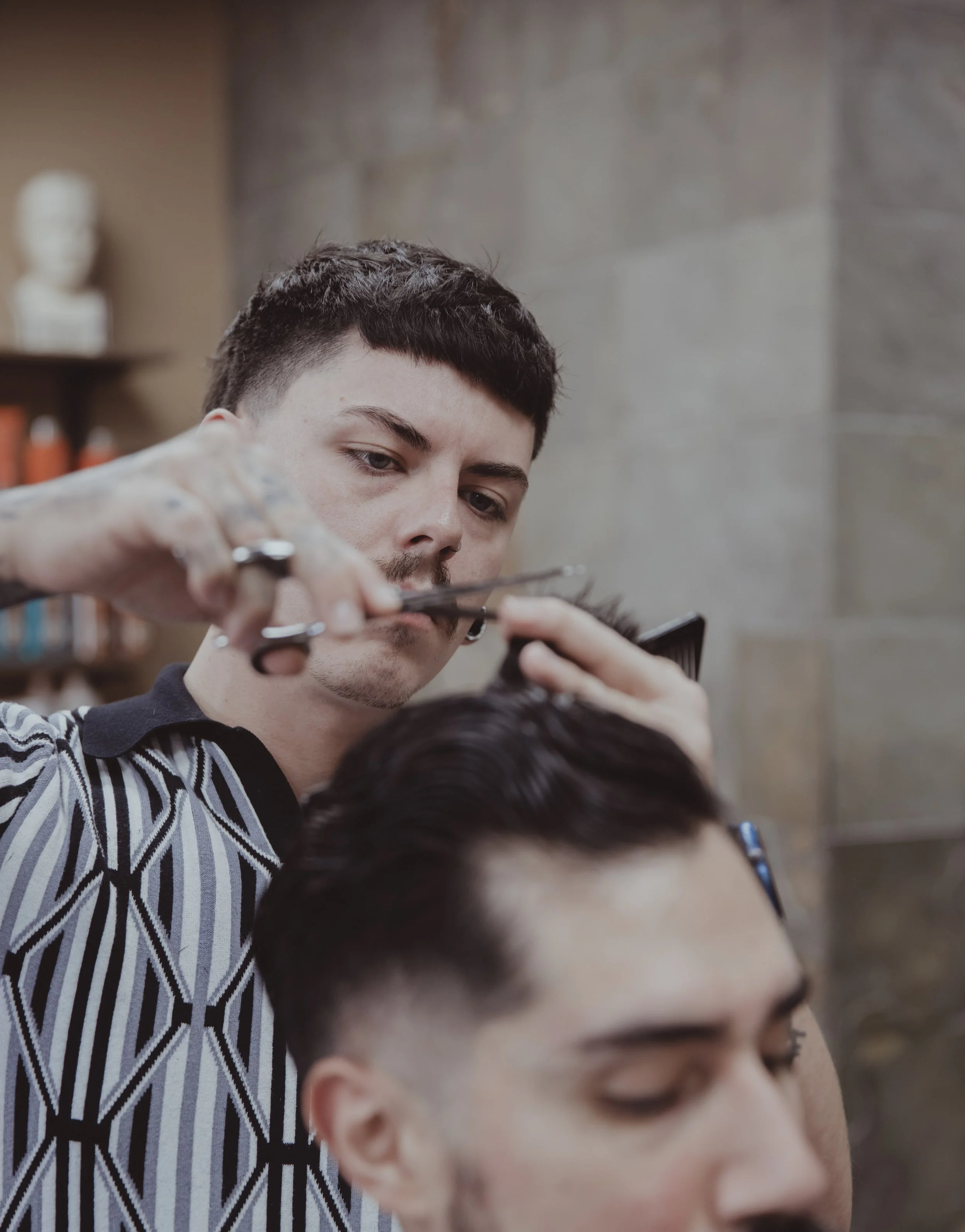 Professional hairstylist cutting a client's hair in a modern barbershop with a focus on precision grooming and contemporary men's haircut styles.