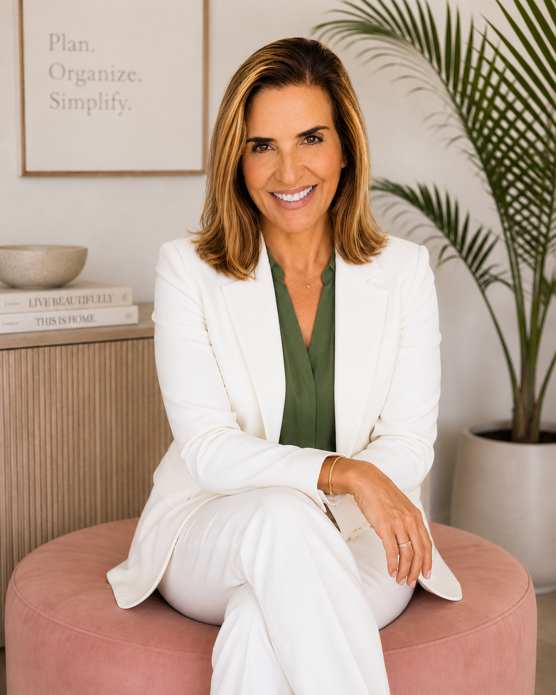 The owner, Heather Lilly, wearing a white suit and green blouse, sitting on a pink ottoman in a modern office.