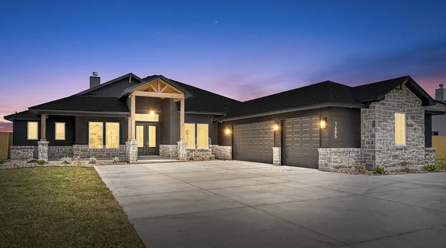 Newly built house with black exterior and attached three-car garage, construction still in progress, in a rural area with cloudy sky.