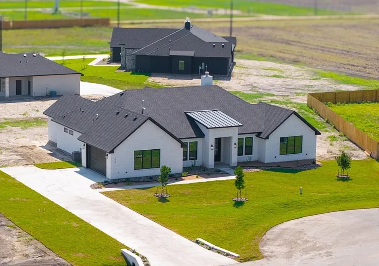 A new, unfinished house with white siding, black window frames, and a dark roof under a partly cloudy sky.