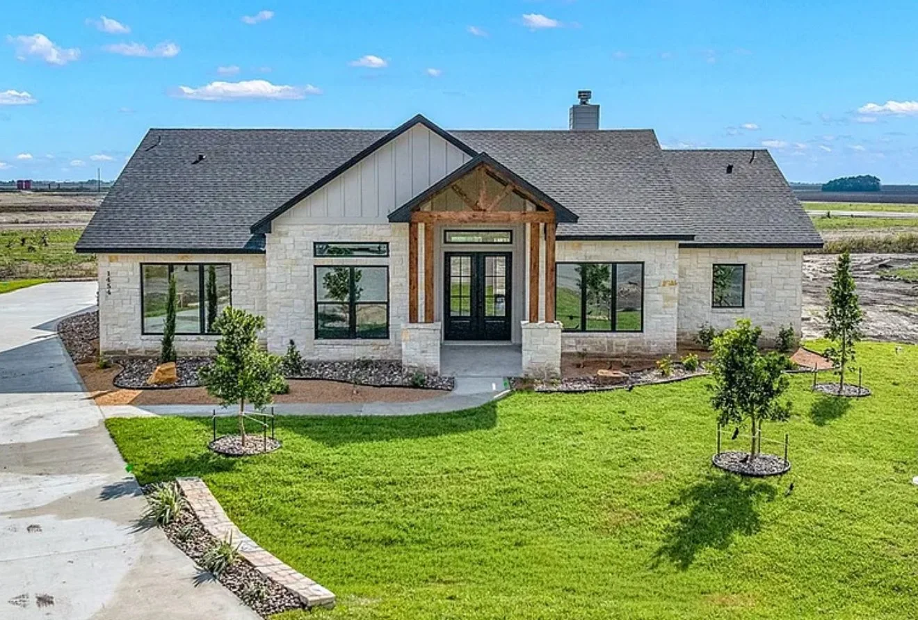 Modern house with stone exterior, large windows, and a front porch with a gable roof, at sunset.