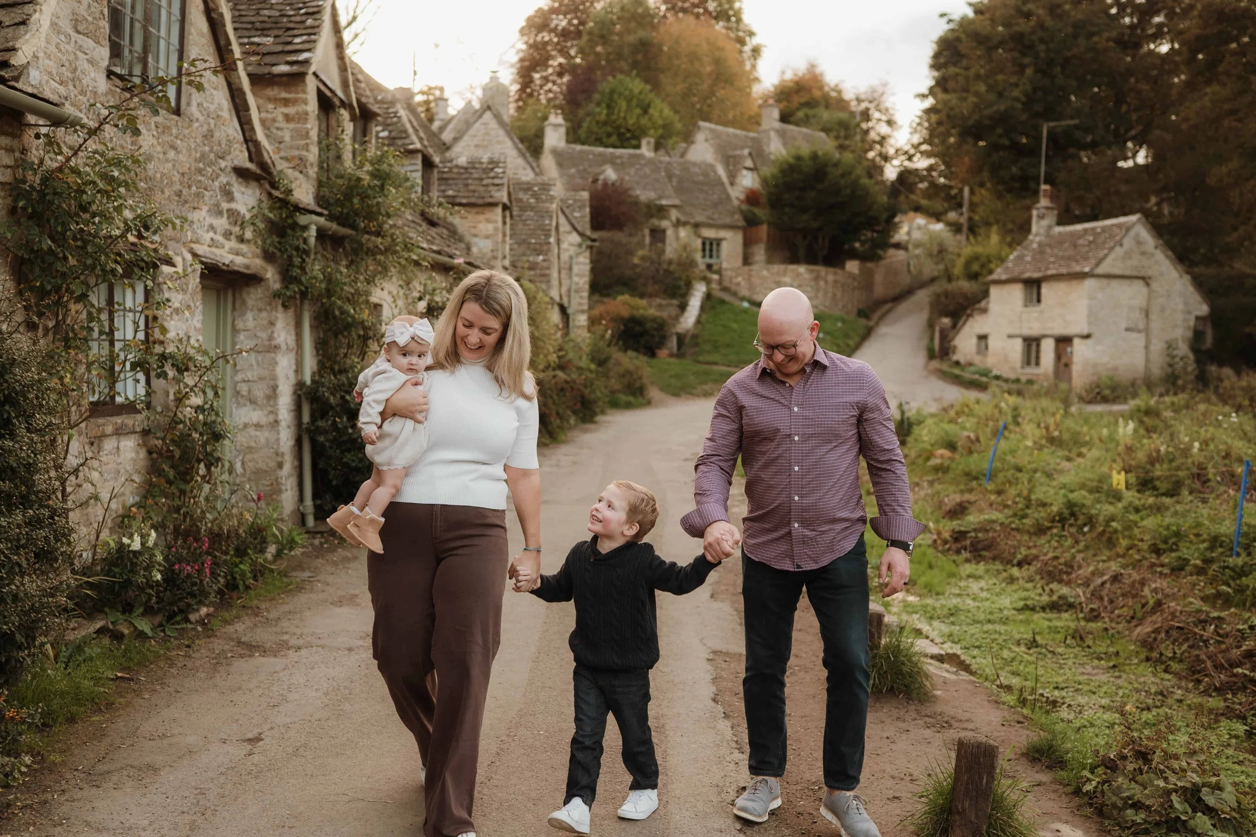 Family of four holding hands on the street of the small cotswold village of bibury at sunset