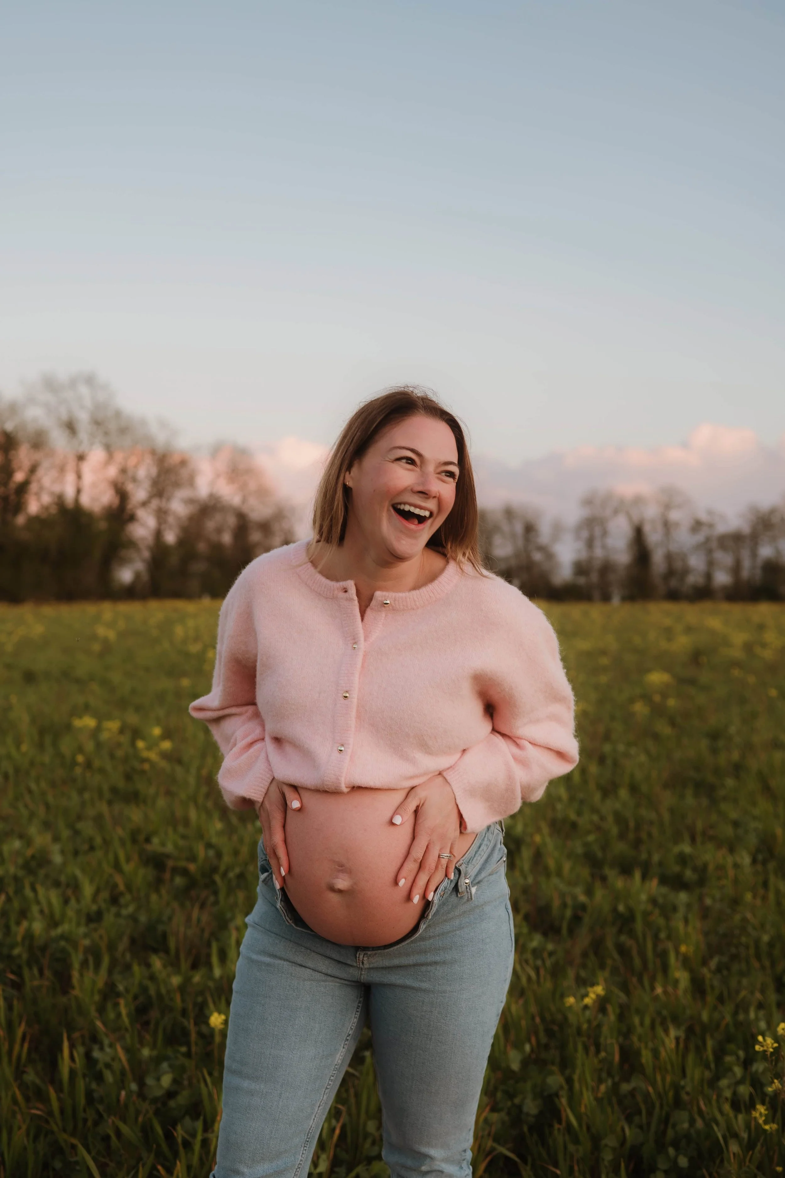 joyful pregnant mother in a field of yellow flowers wearing a pink cardigan and jeans