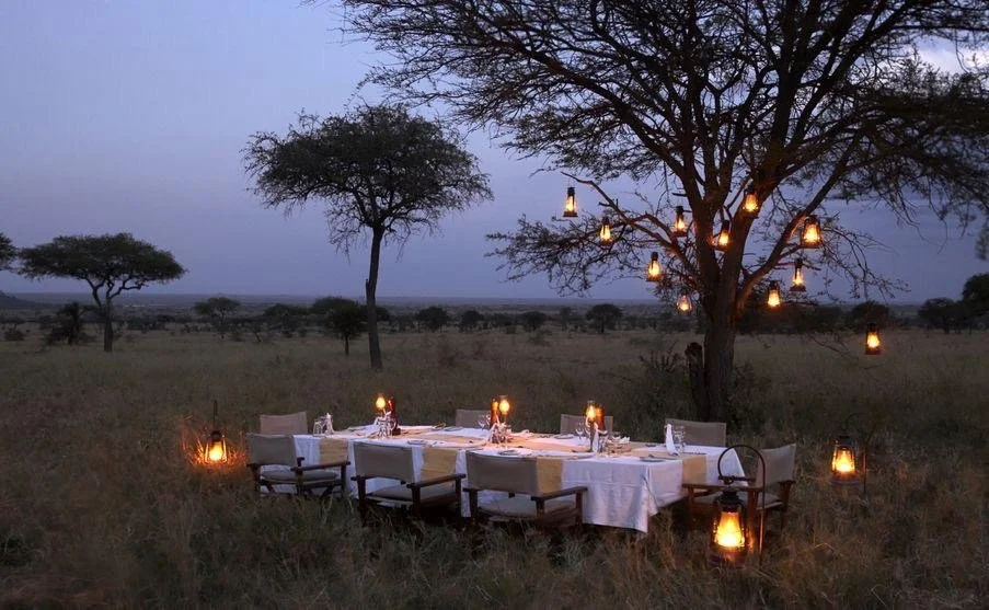 Dining table set in the outdoors during at dusk with lanterns all around