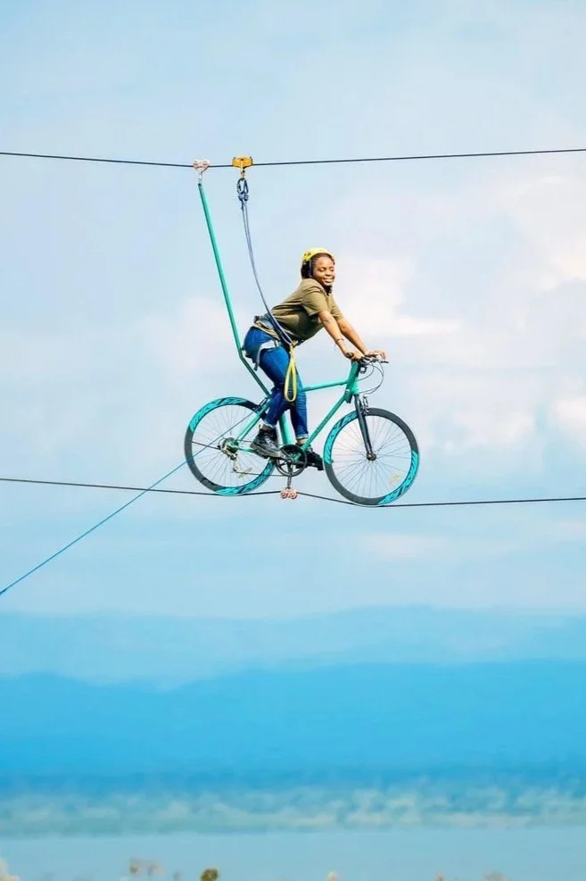 A smiling woman riding a sky bike across a wire