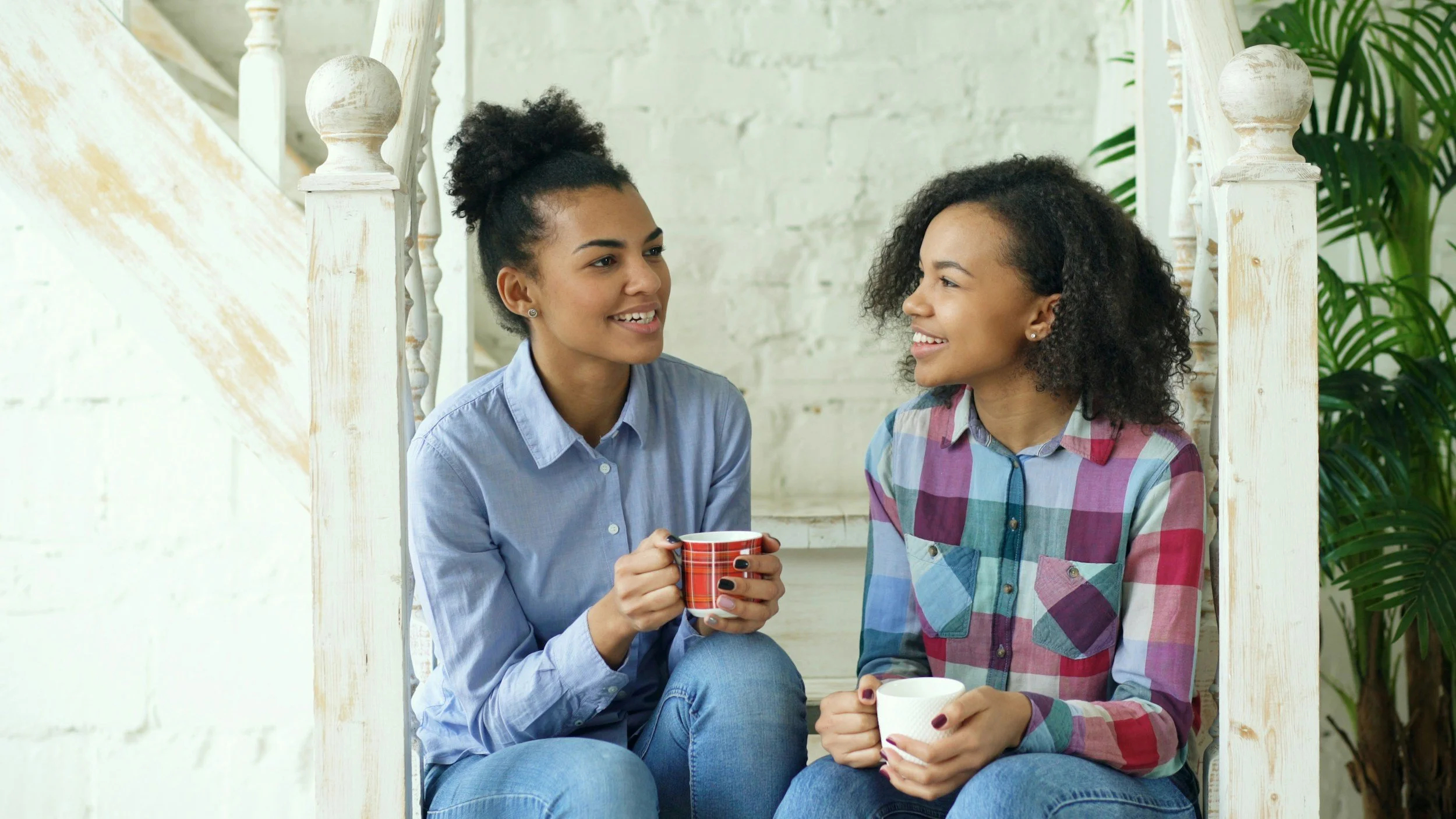 Two women sit on stairs talking to each other, indicating the importance of communication while Uranus is in Gemini.