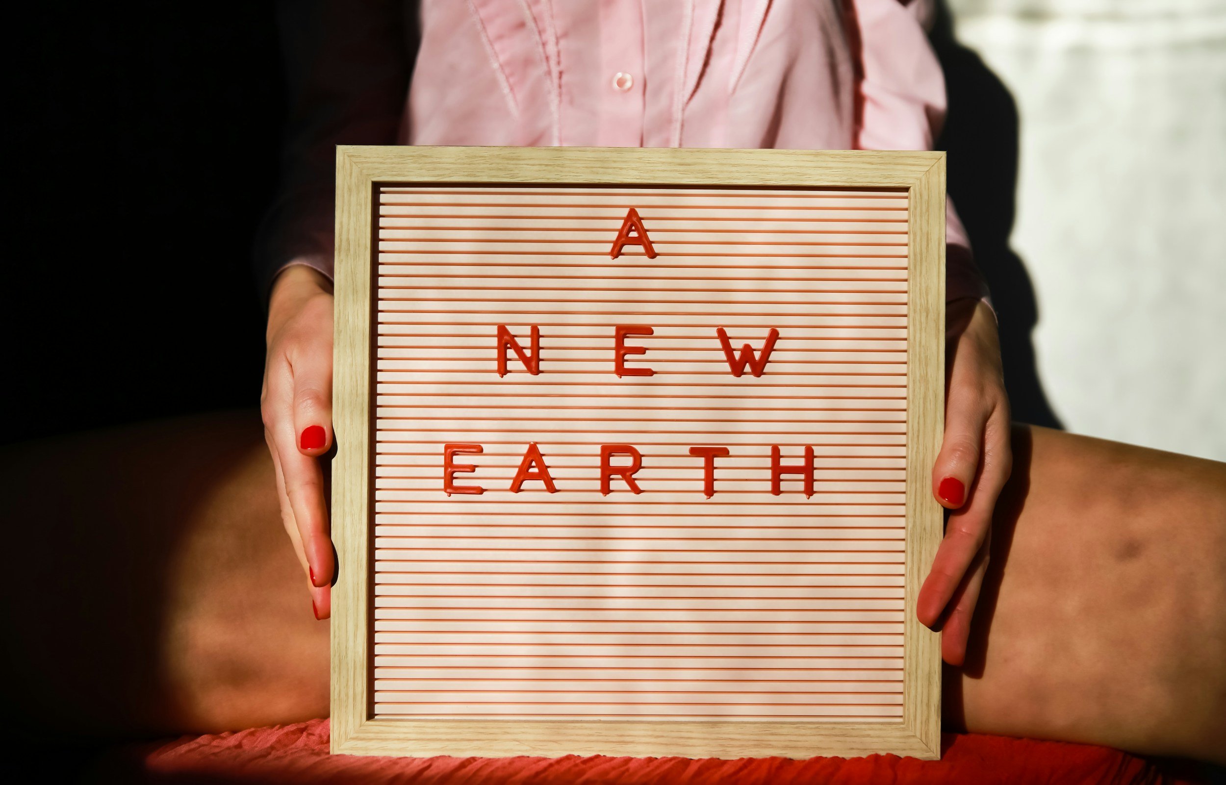 A woman holds up a letter board which reads, "A New Earth," symbolizing the new beginnings stemming from the Saturn and Neptune in Aries conjunction.