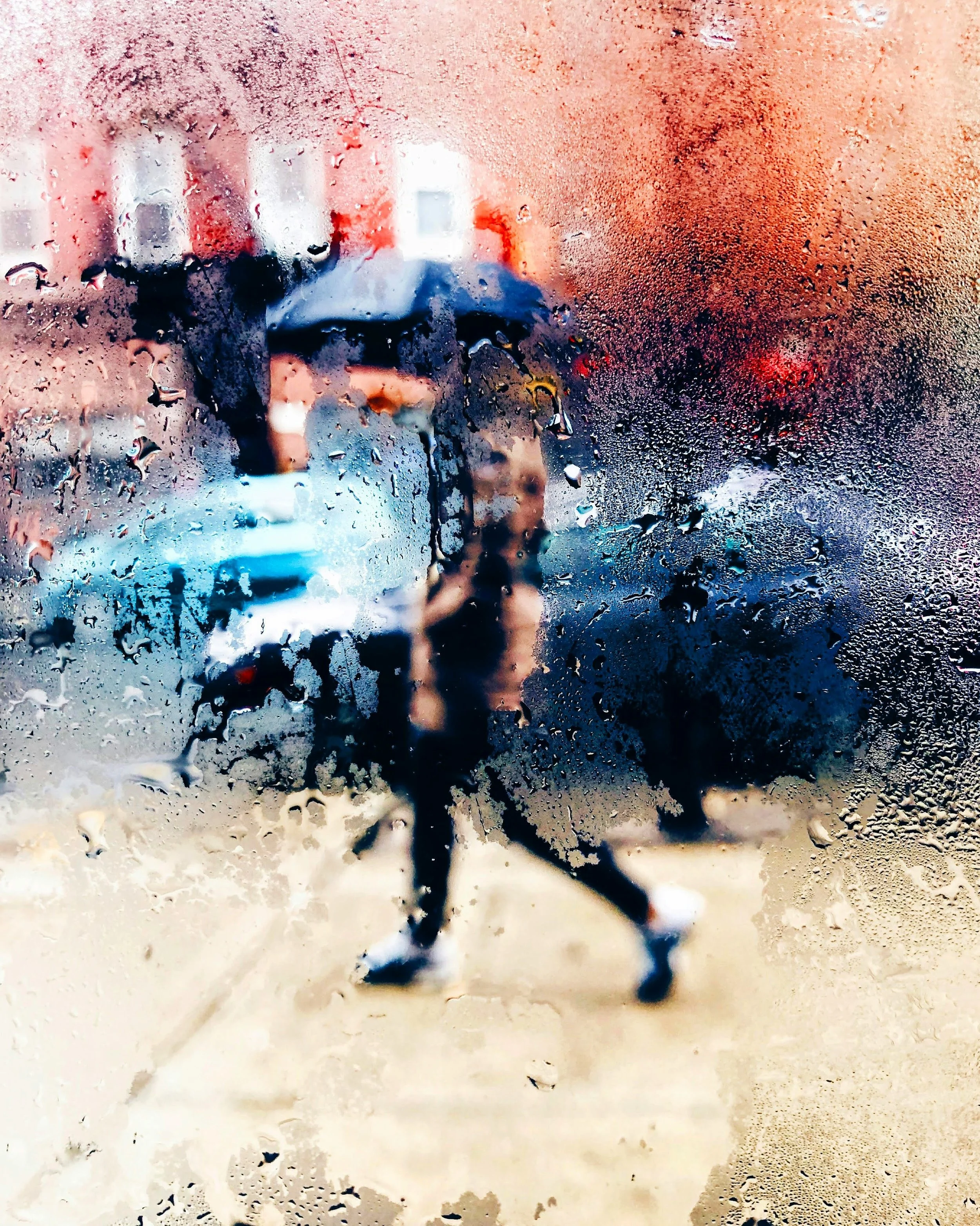 Photo of woman walking in NYC street with umbrella, taken from inside through blurry storefront window.