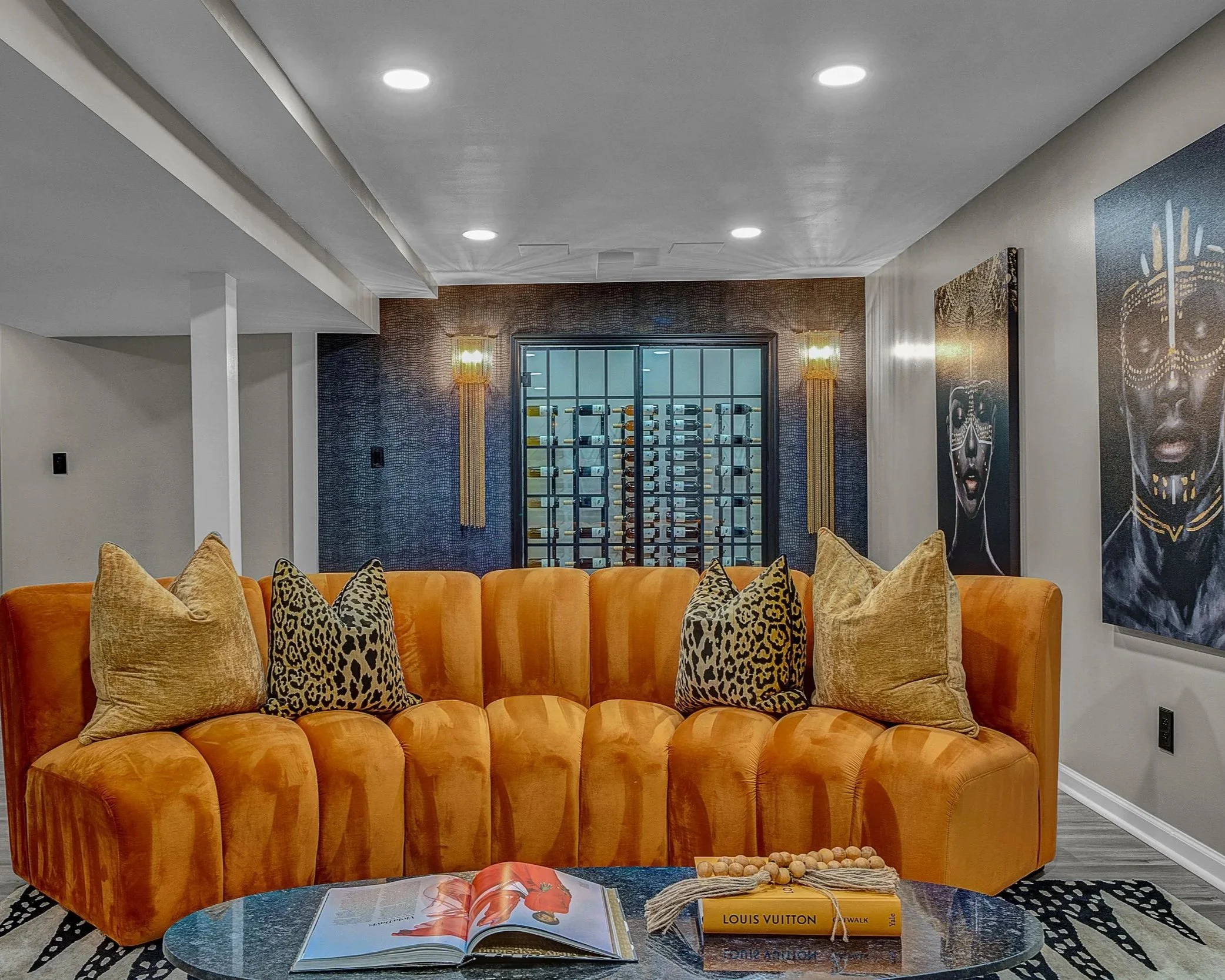  Lower-level basement lounge is bold, moody, and effortlessly luxurious. A sculptural orange velvet sofa becomes the showstopper, paired with textured wallcoverings, dramatic art, and statement lighting for an elevated, cinematic feel. The glass-fron
