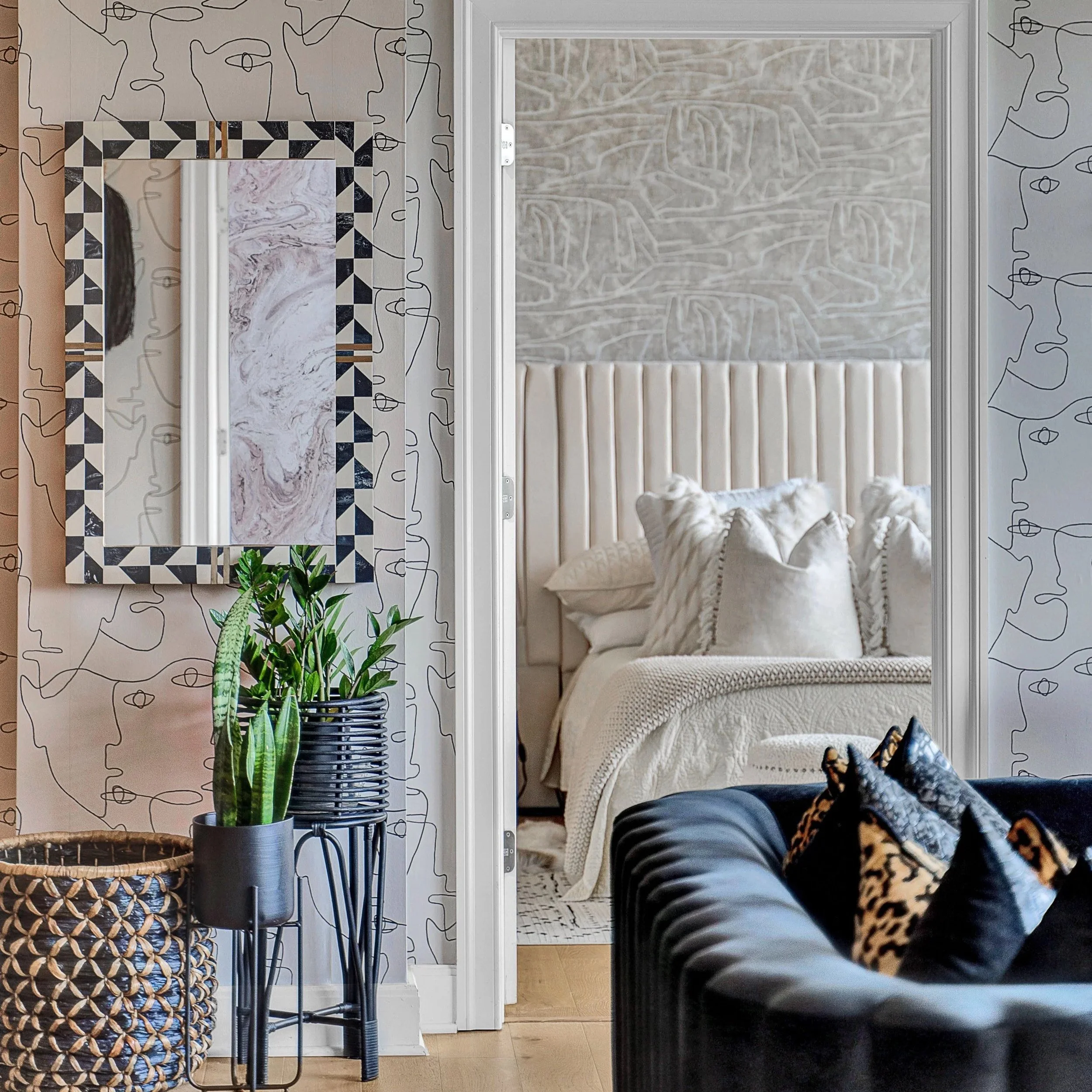 This image showcases a beautifully curated vignette featuring modern, sculptural furniture and soft, layered textures. A graphic black-and-white accent chair with bold leopard-print pillows adds drama in the foreground, while a trio of stylish plante