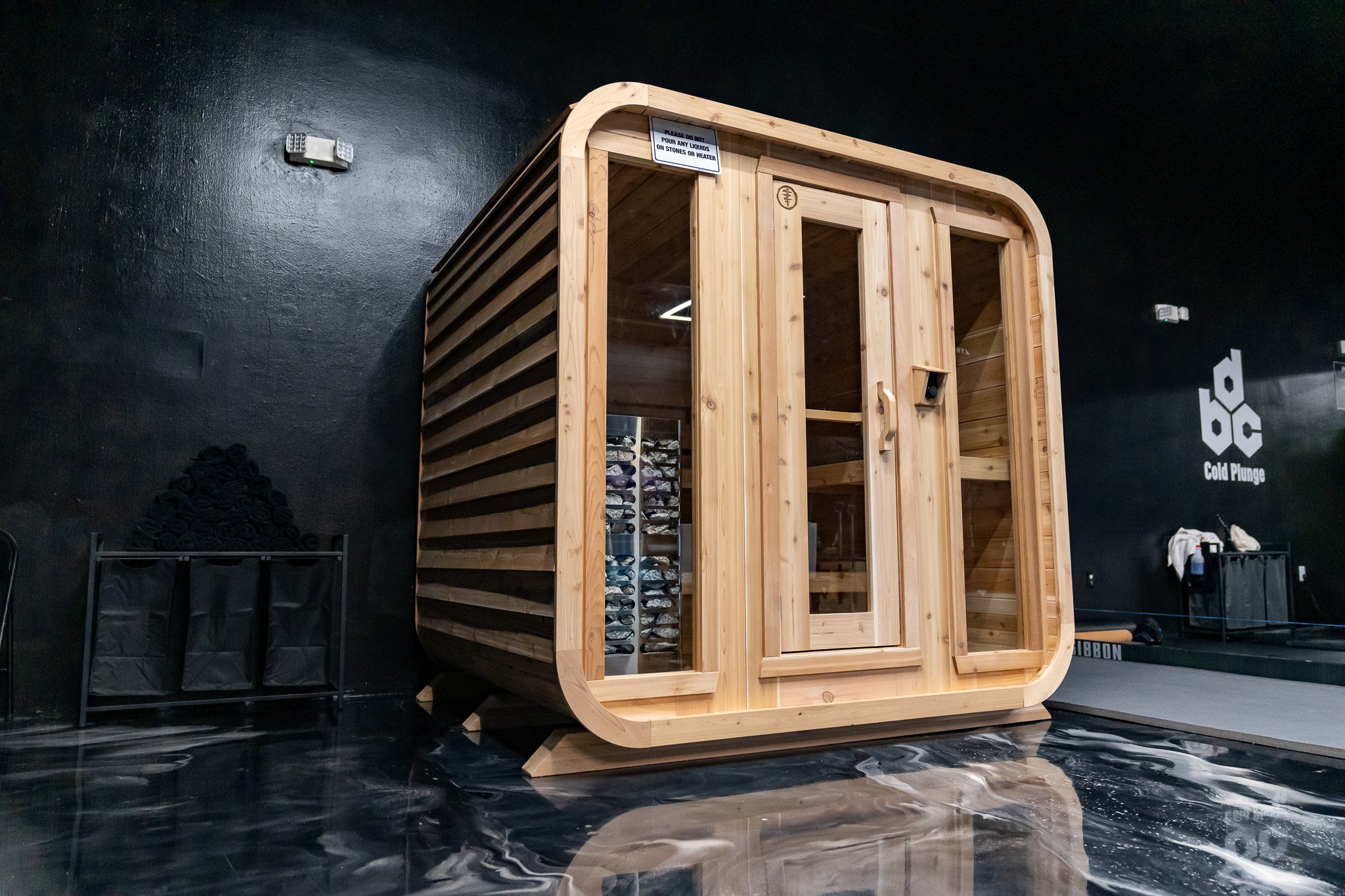 Indoor temperature-controlled sauna made of light wood with glass door, located in a gym or wellness center.