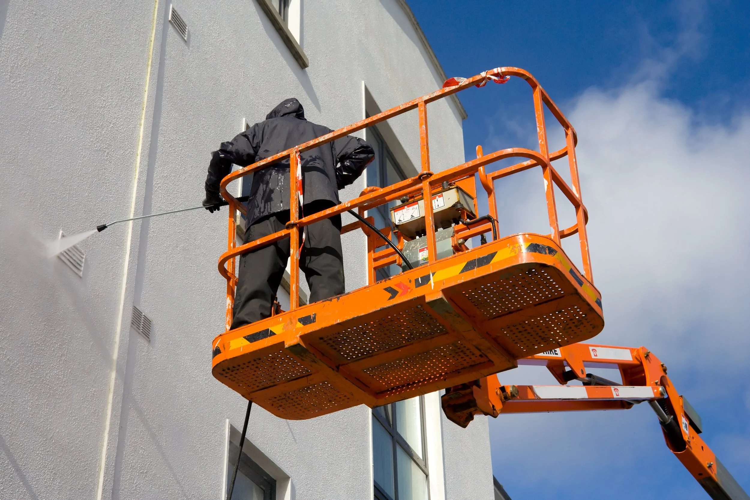 Man in crane power washing building.