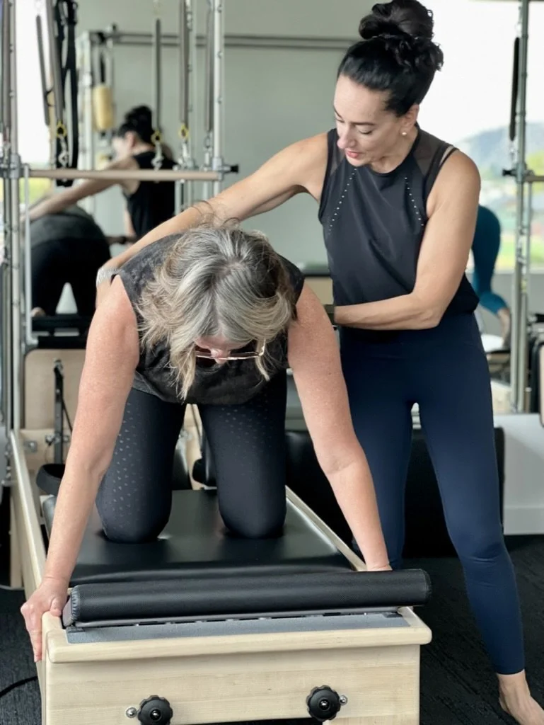 Pilates instructor assists client with her form during a session