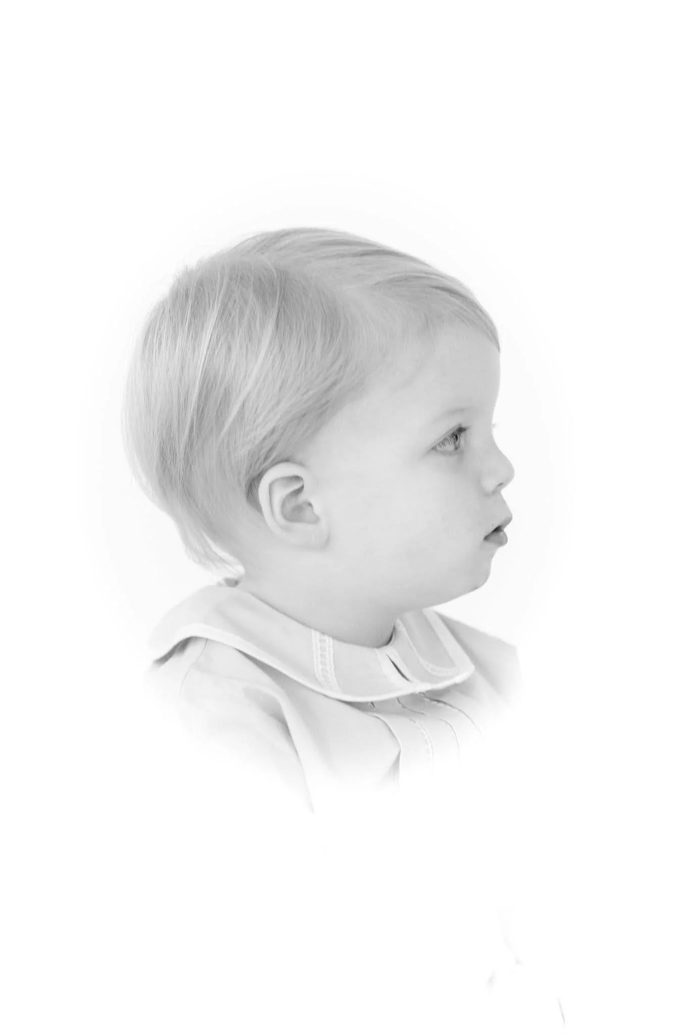 Young girl with blonde hair and blue eyes, wearing a light-colored dress and a white bow in her hair, smiling softly against a white background.