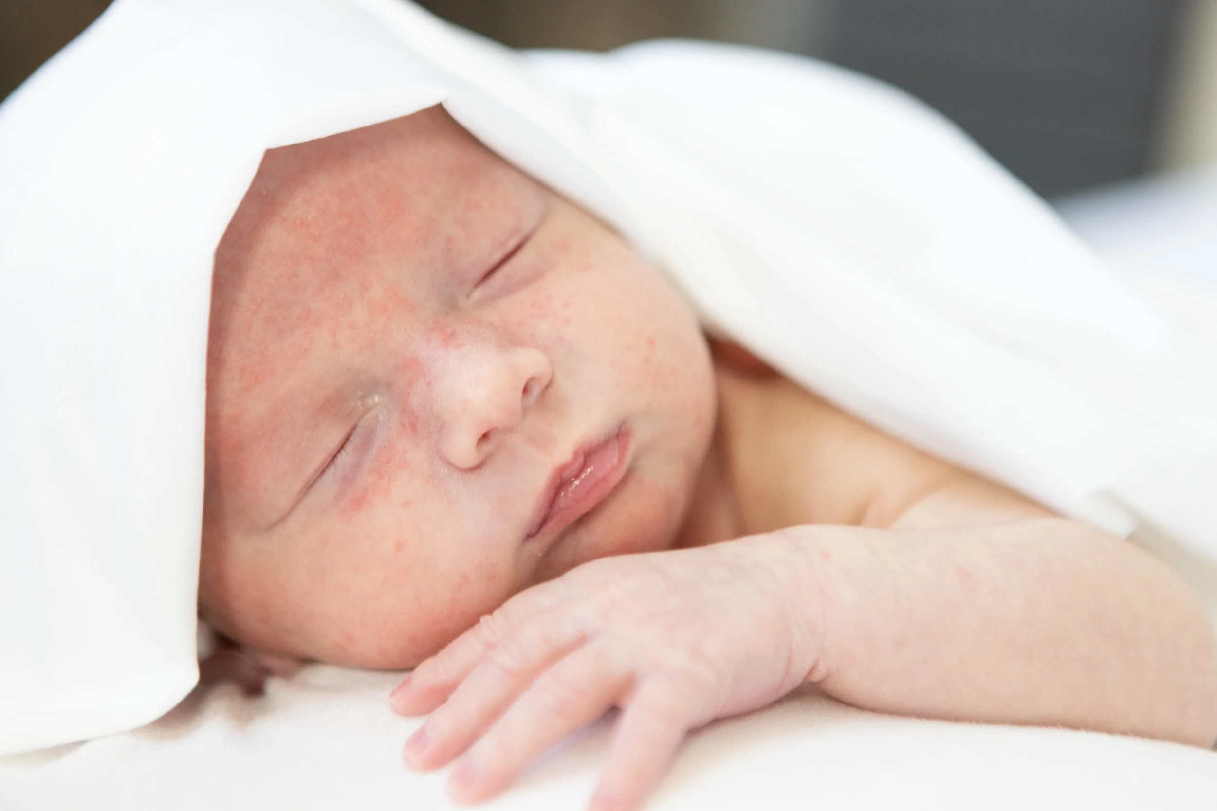 Close-up image of a sleeping newborn baby with a blanket covering part of their head and arm.