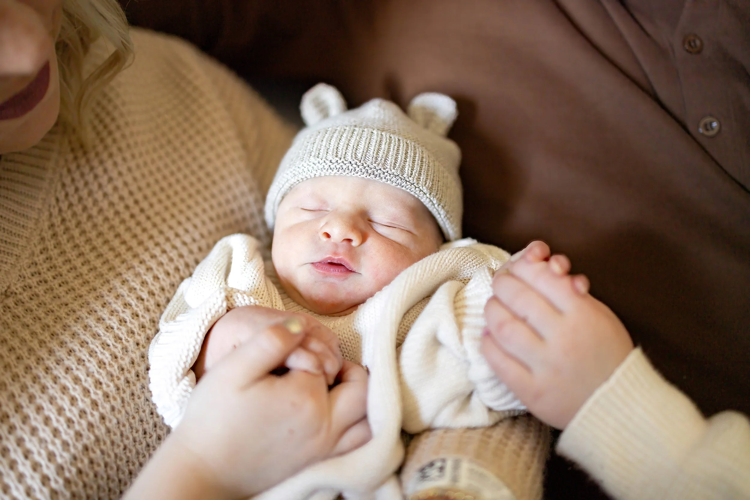 A collage of photos from a newborn's birth and hospital stay. It includes a newborn baby in a hospital bassinet with a name tag, the baby in a hat with 'pax' written on it, a mother and her young son holding a tiny newborn, the newborn sleeping in a hospital bed with hands gently touching, the parents holding the newborn in a hospital room, and the family sitting together in the hospital room with a hospital bassinet in the background.