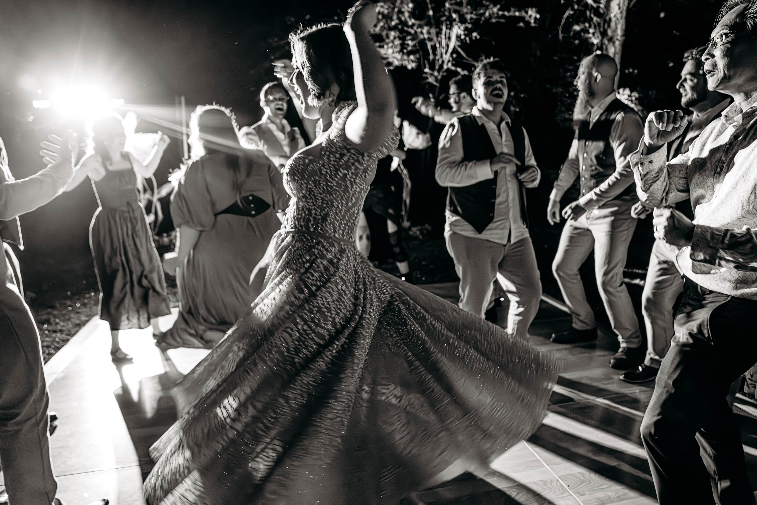 People dancing at an outdoor party at night with bright light in background, black and white photograph