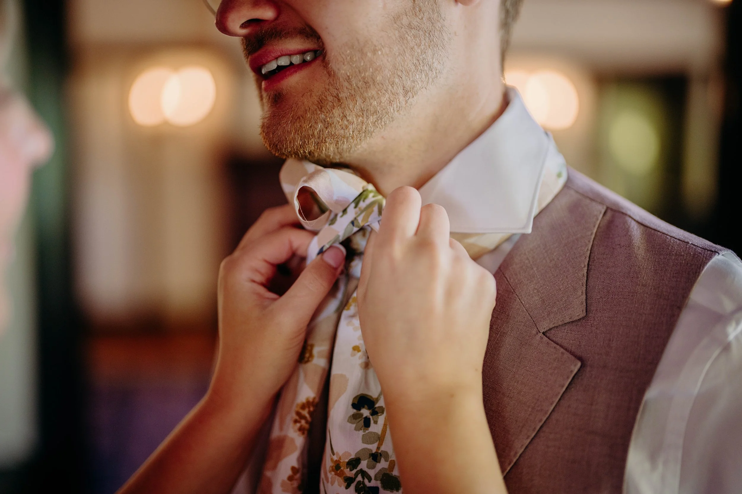 A woman adjusting a man's floral-patterned tie at a formal event.