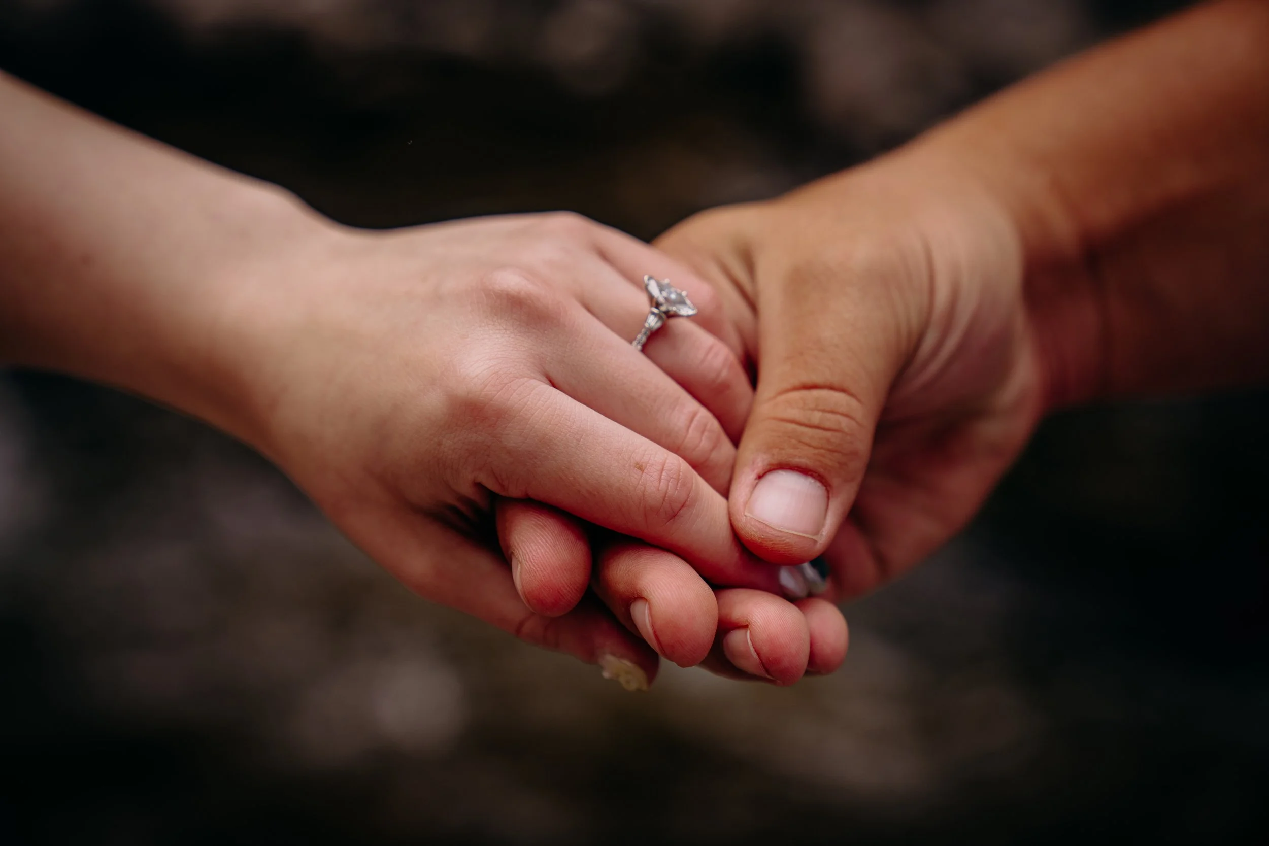 Close-up of a man and woman holding hands, with the woman wearing an engagement ring.