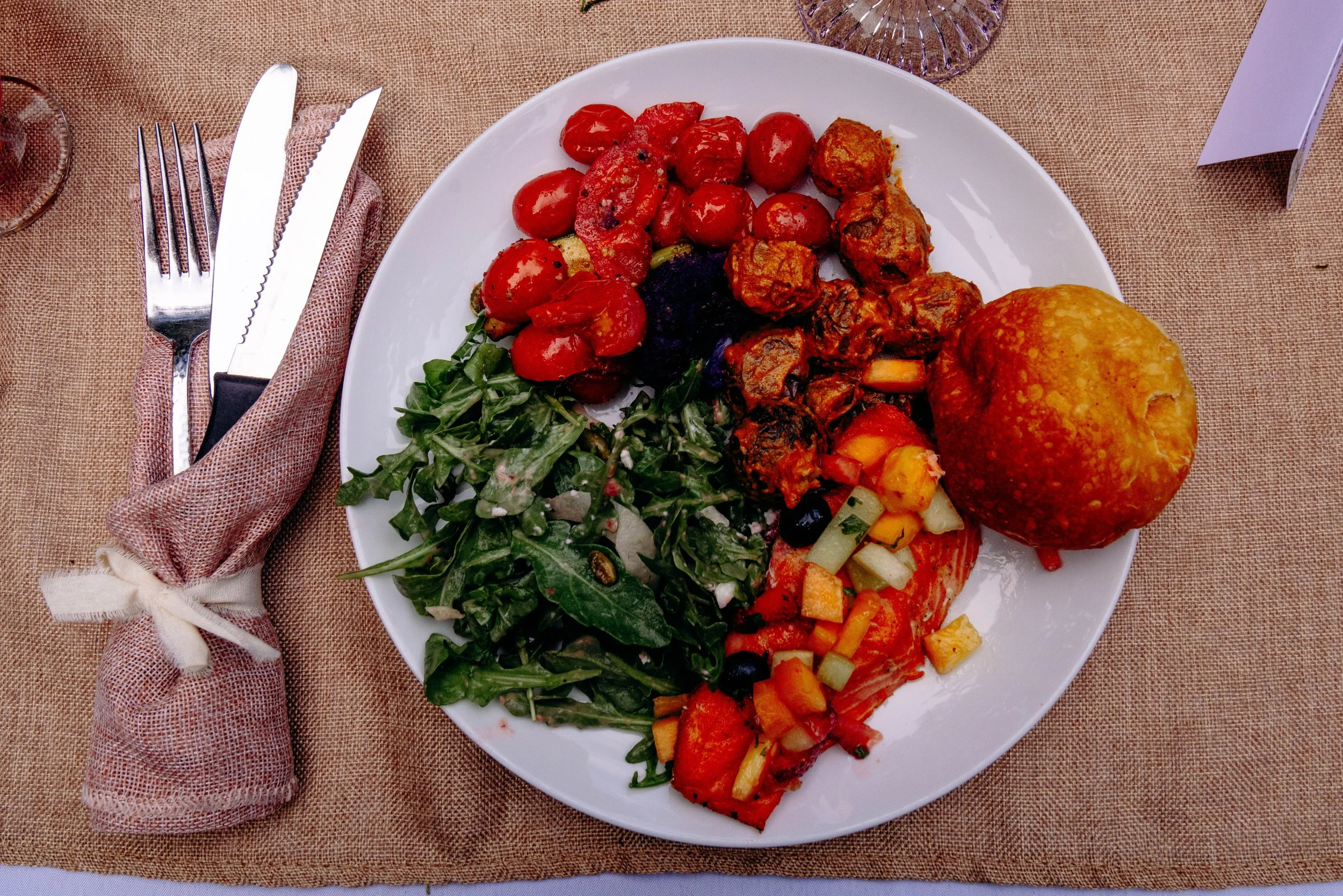 A white plate of mixed vegetables and a large baked cornbread muffin on a brown tablecloth.
