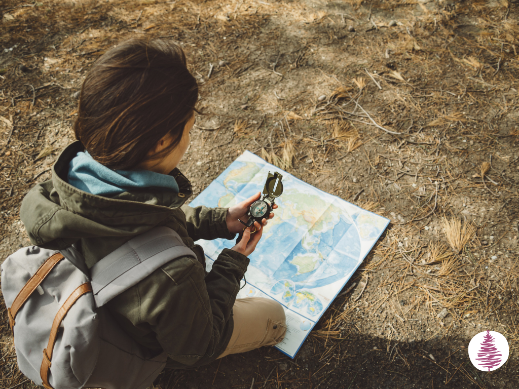 A woman in outdoor gear kneels on the ground with a compass and amap