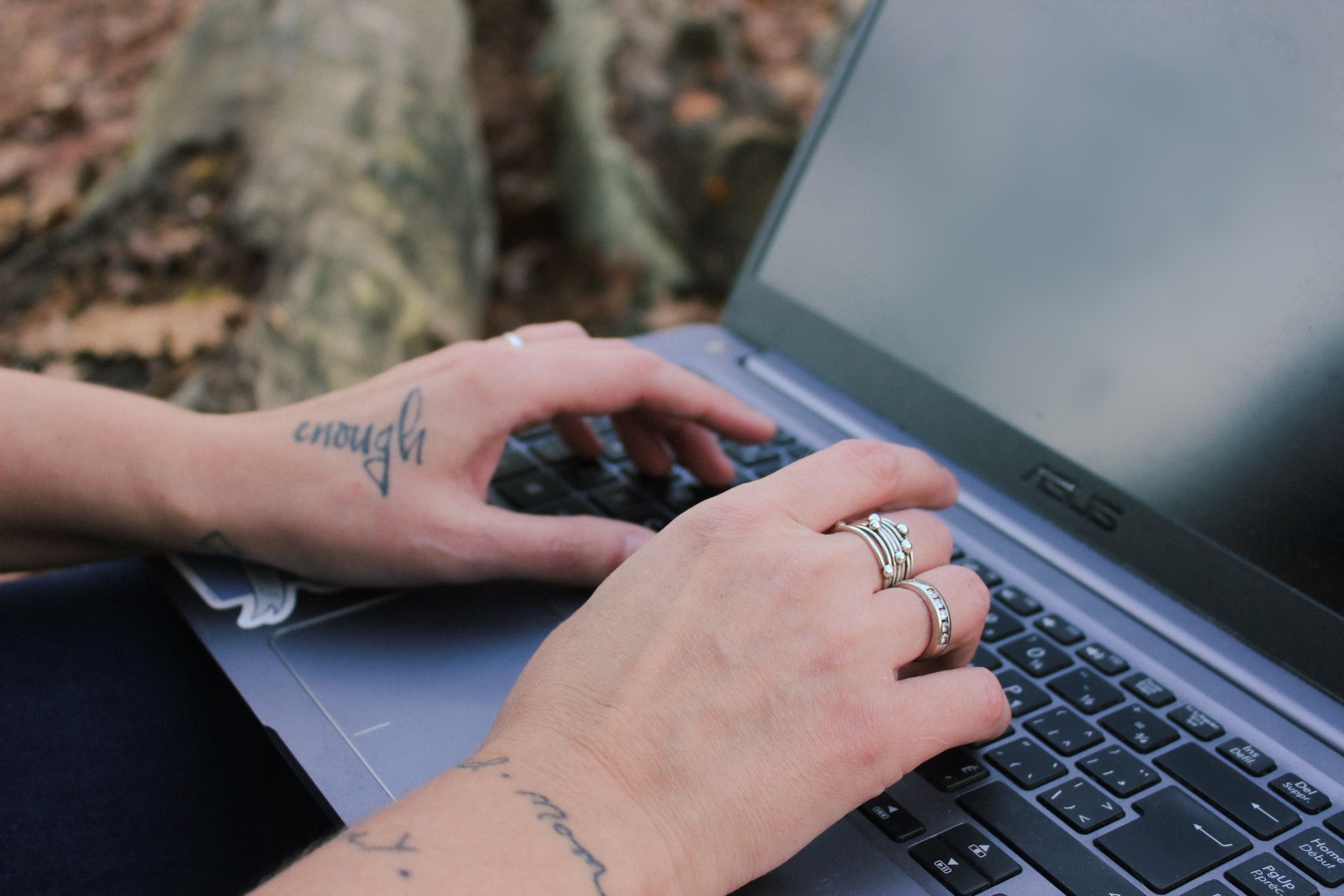 Hands with silver rings and tattoos on a laptop keyboard