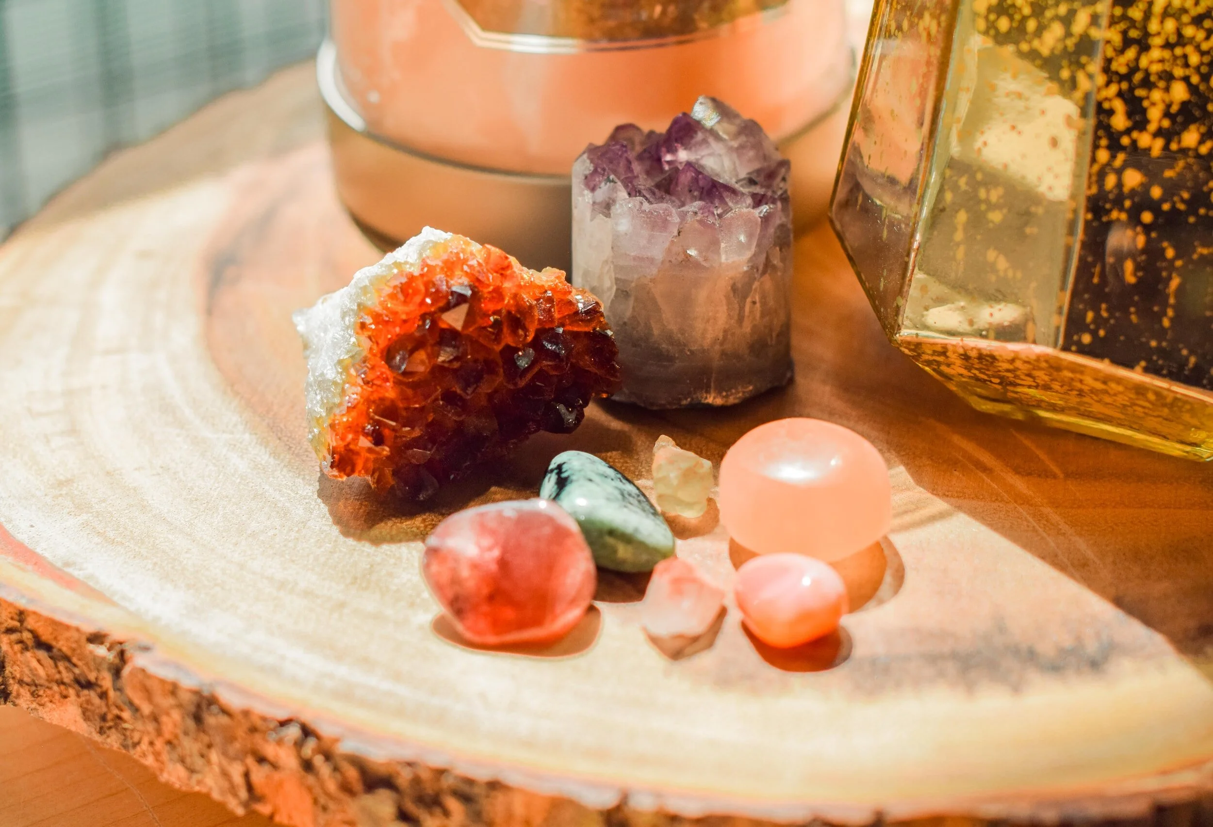 Various colorful crystals and gemstones placed on a wooden surface, with a metallic container and a glass box in the background.