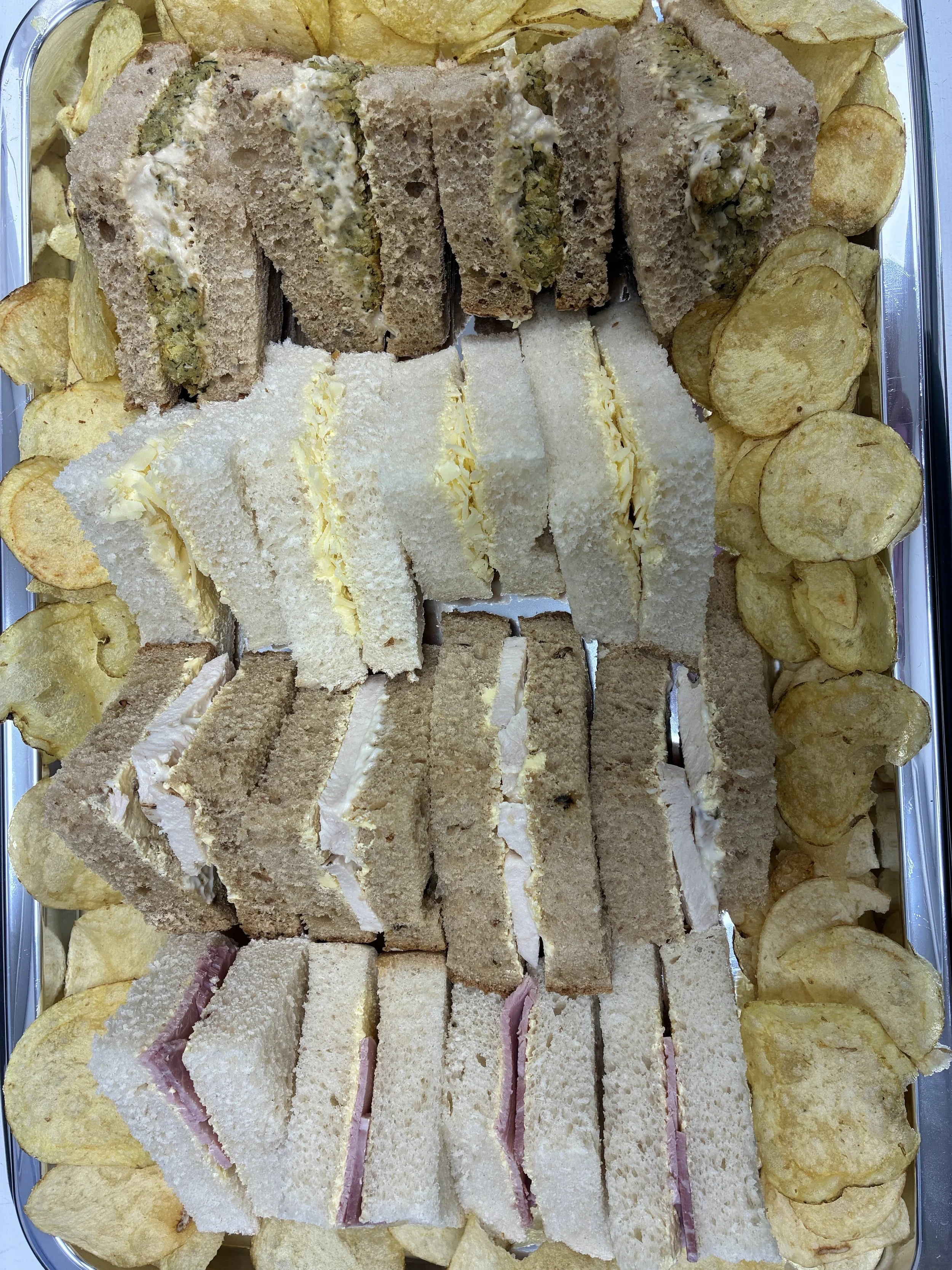 A tray of assorted finger sandwiches with potato chips around the edges.