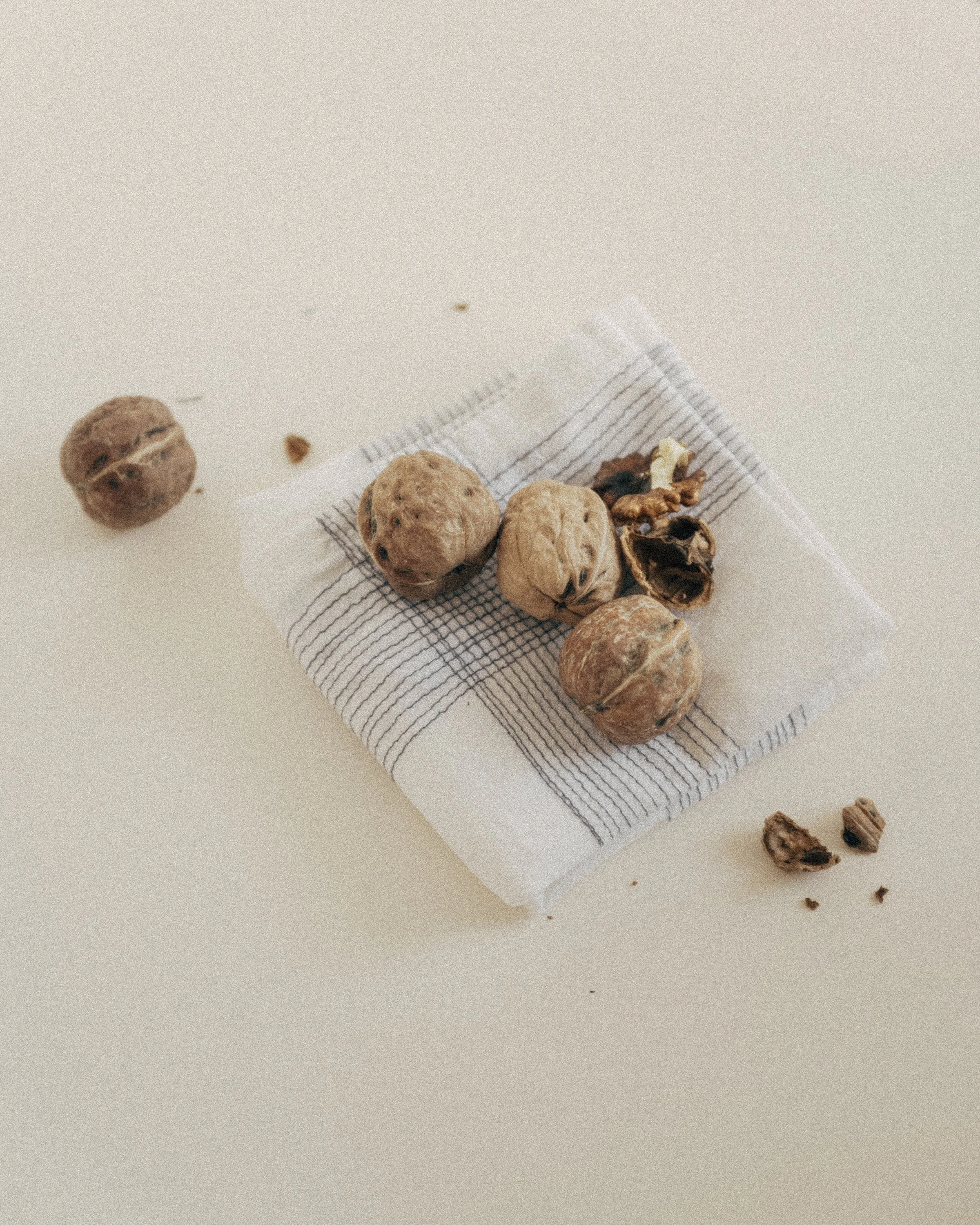 Whole walnuts and cracked shells on a folded linen cloth with thin grey stripes.