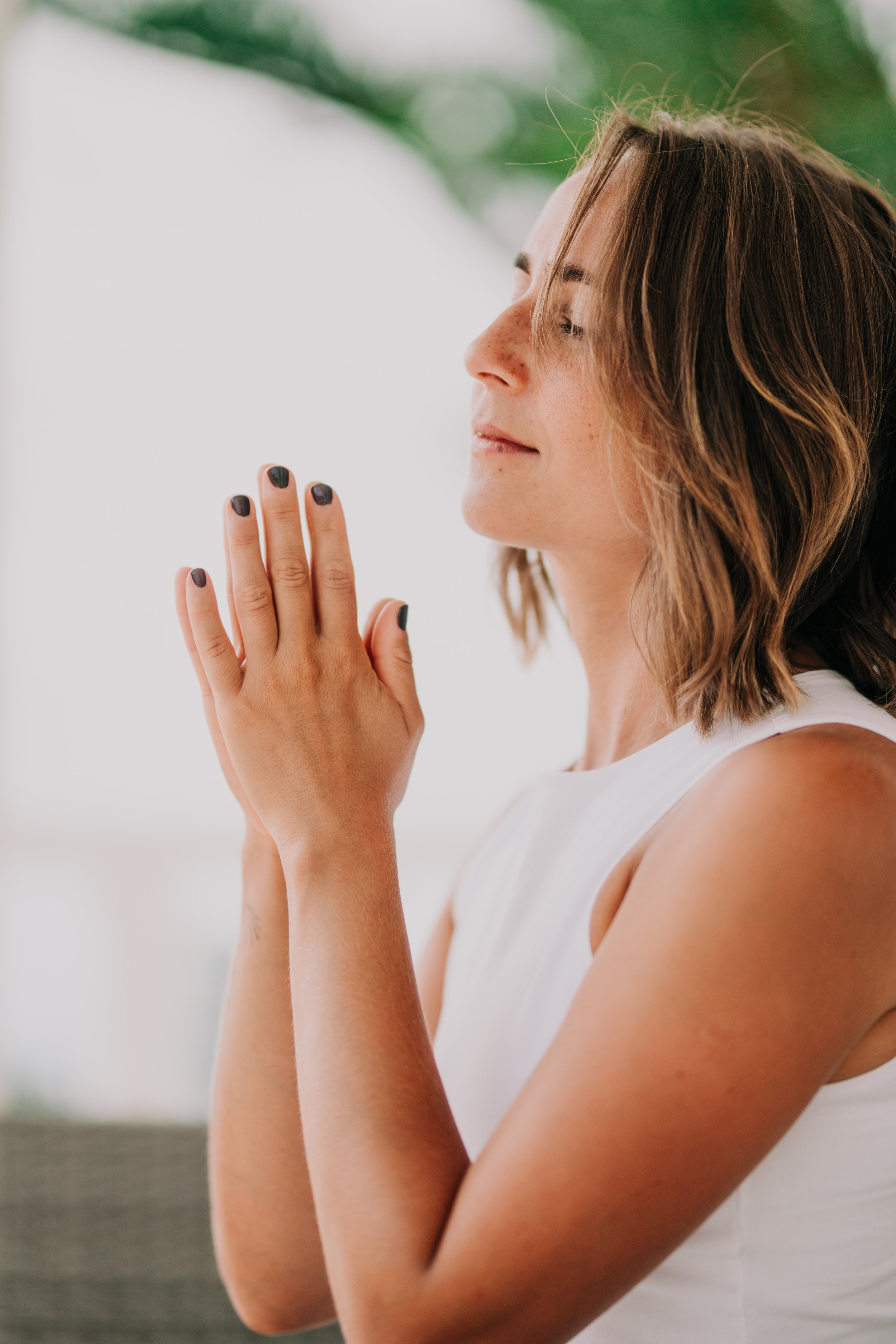 Woman with hands in meditation prayer in front of a clean wall