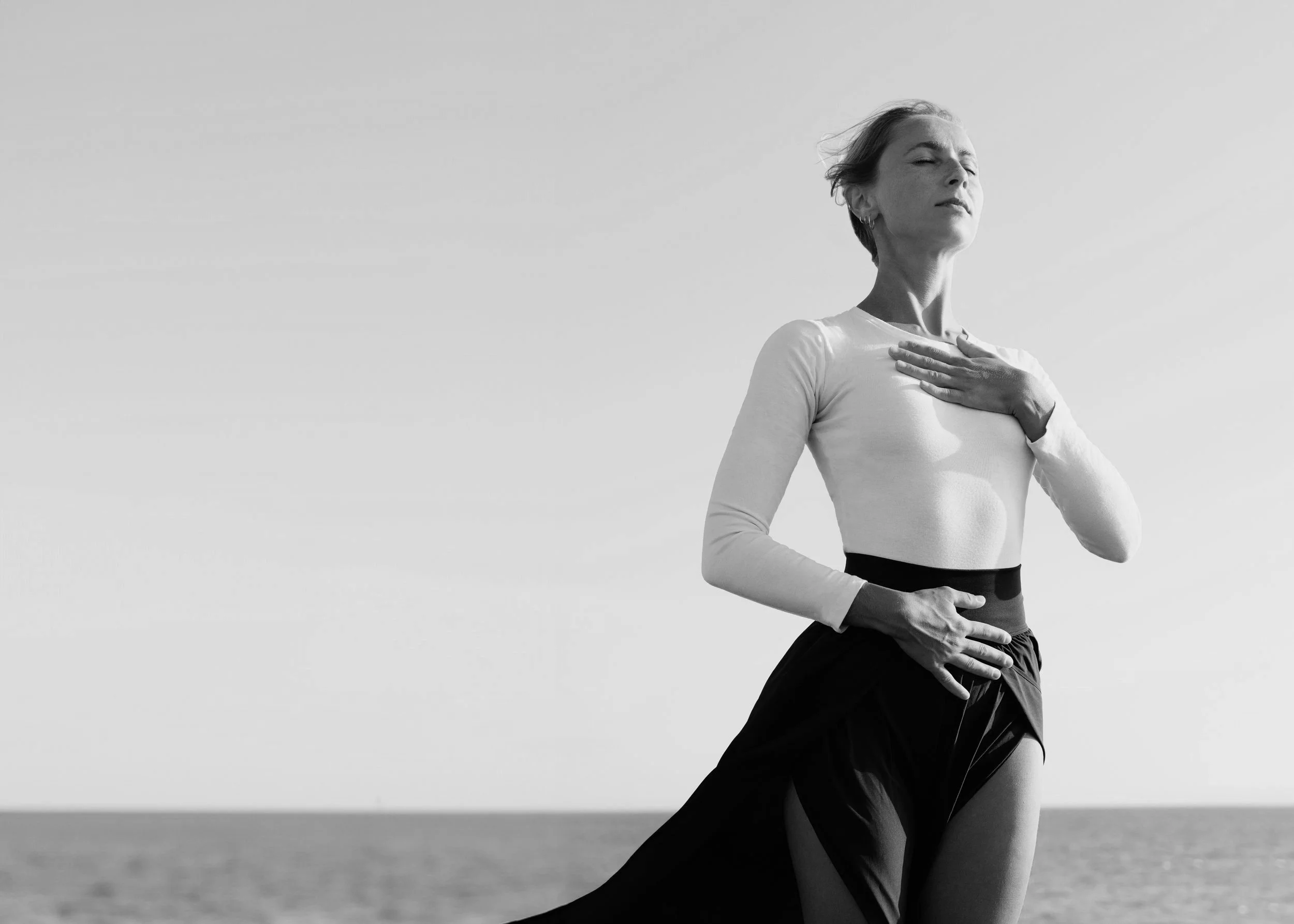 Woman holding her hands on her heart and adomen, closing her eyes with the ocean in the background