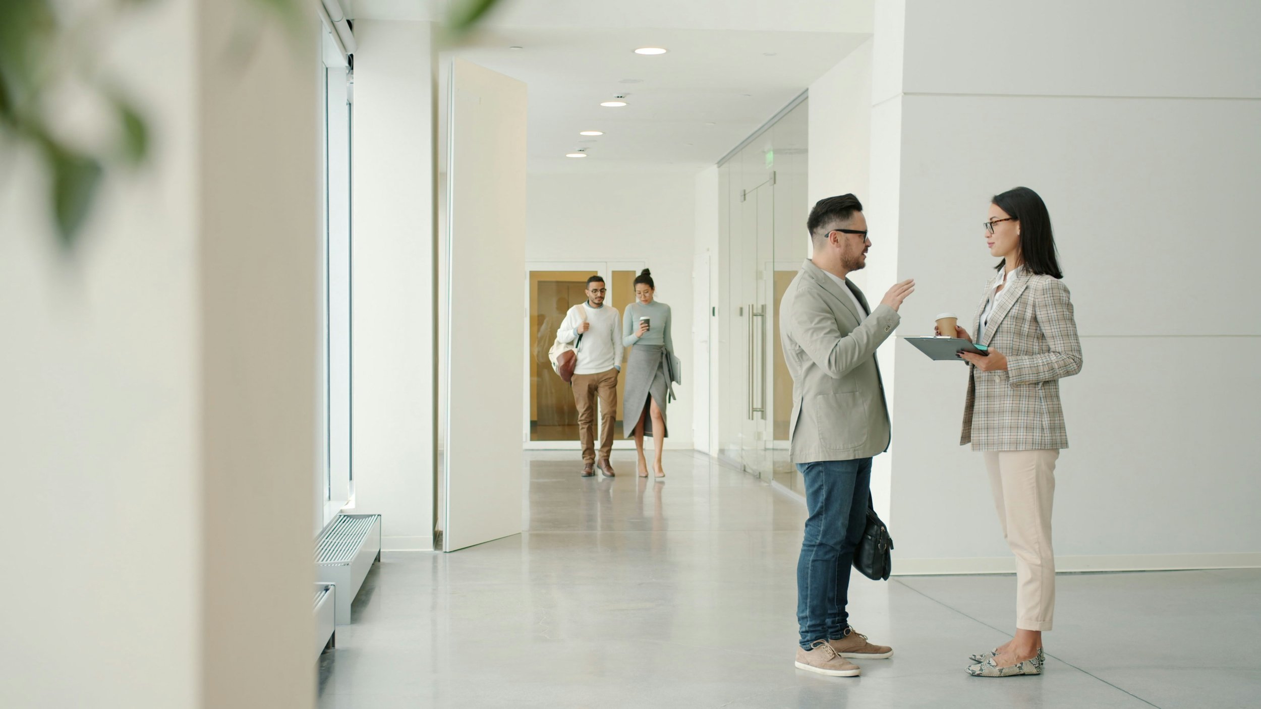 Two colleagues having a private conversation in a modern office hallway, representing how to talk about mental health at work