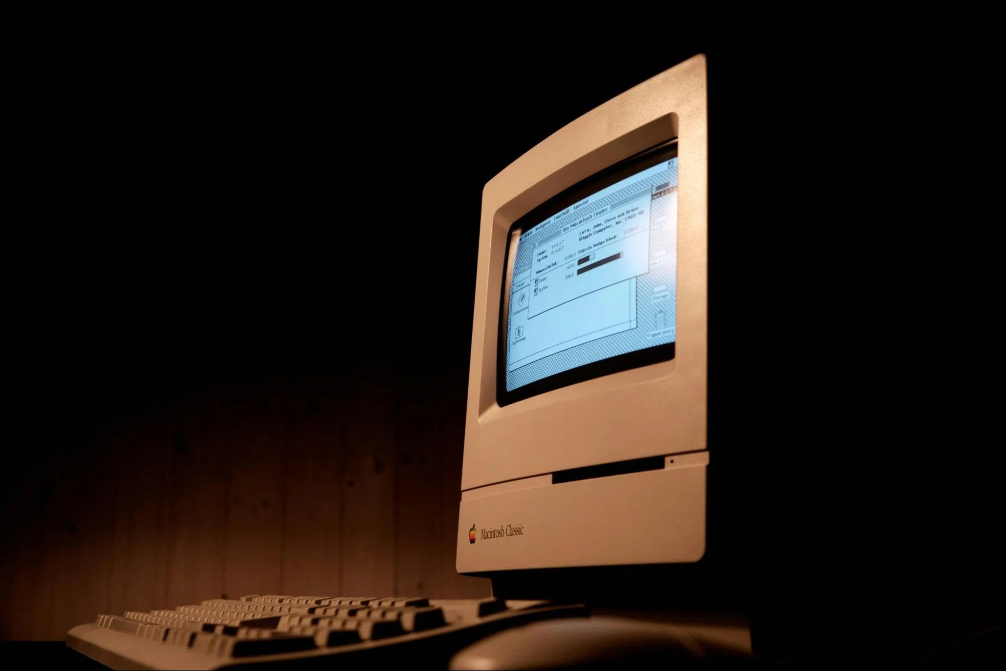 Old version of Macintosh Apple computer monitor and keyboard against a dark background.