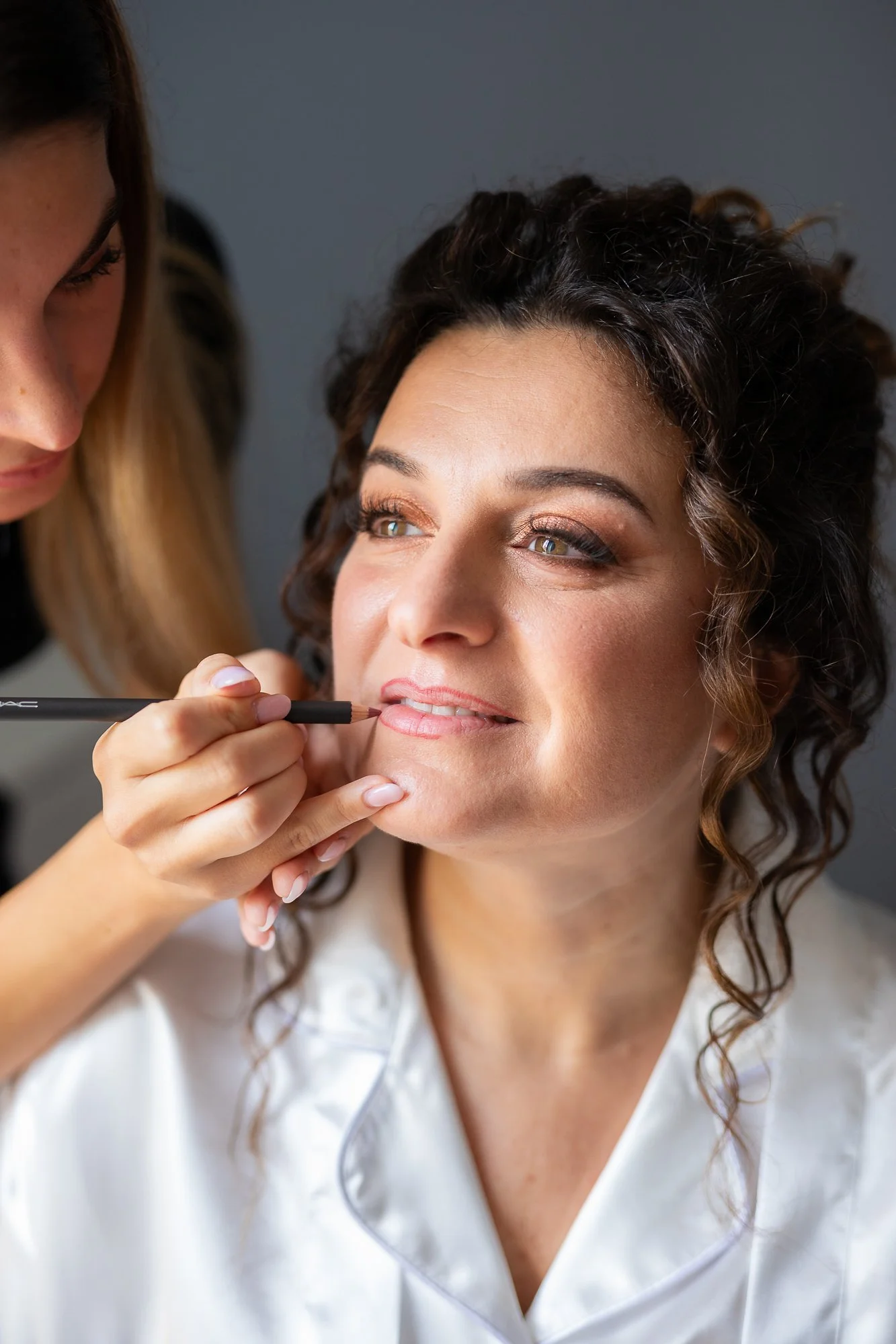 Makeup artist applying lipstick to a woman with curly hair