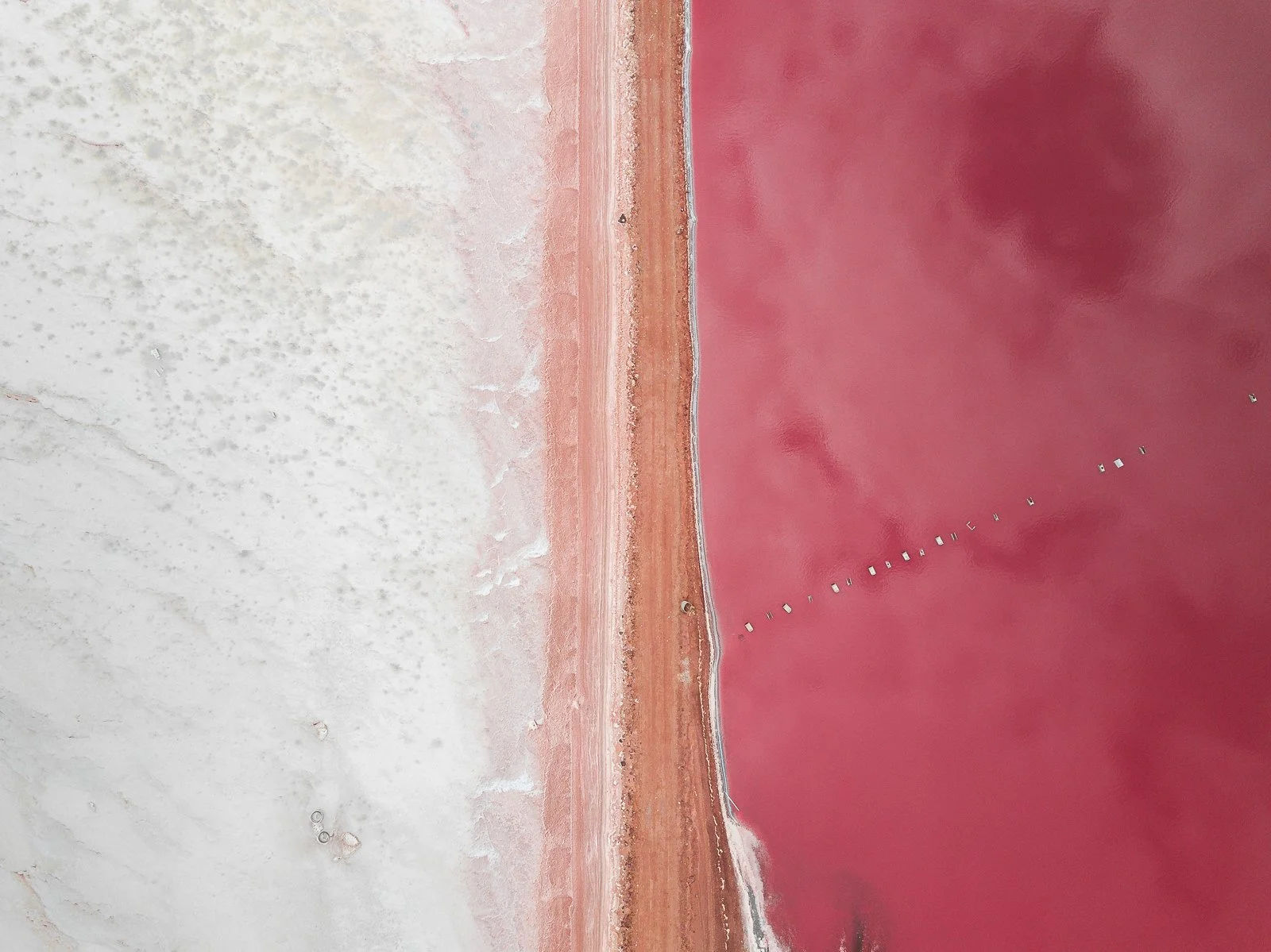 Aerial view of a pinkish salt lake with a shoreline dividing the lake from white salt flats.
