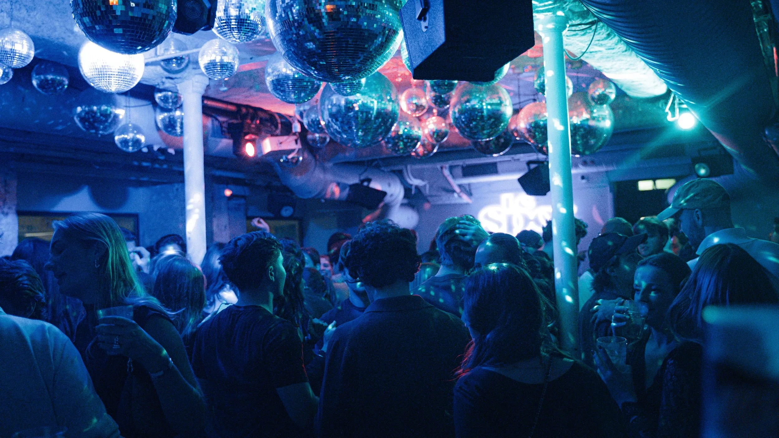 Une foule de personnes dans une boîte de nuit, éclairage bleu et décor de ballons disco suspendus au plafond.