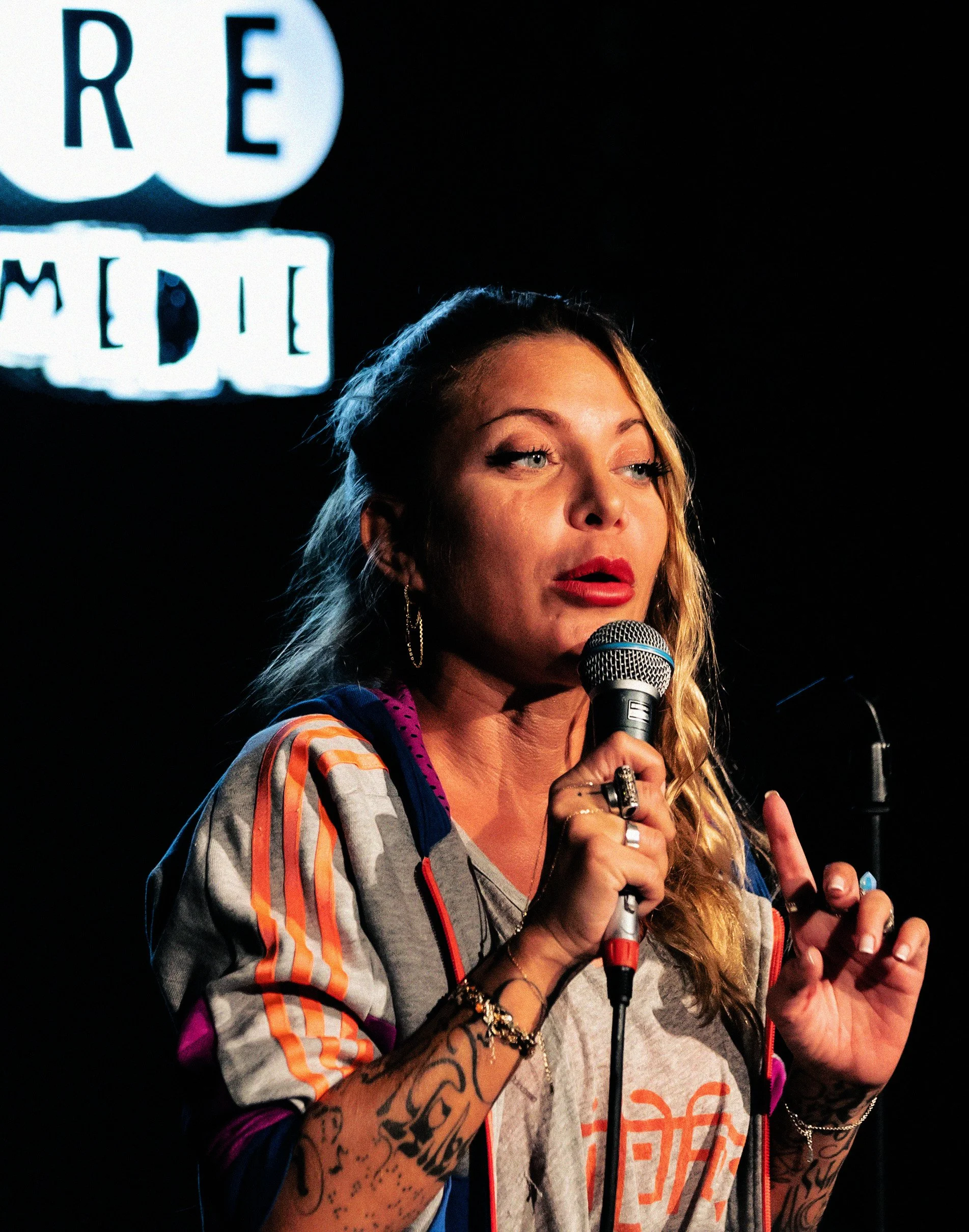 Une femme souriante parle dans un microphone lors d'un événement, avec un logo siglé 'RE MEDIA' en arrière-plan.