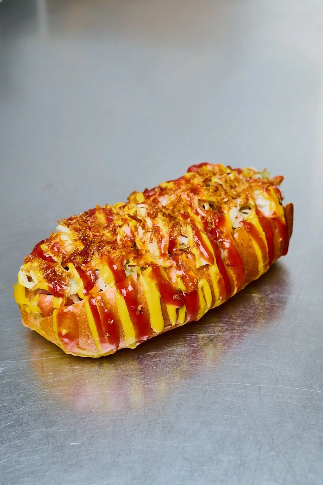 Snack chaud en forme de rouleau, garni de sauce, de fromage, de viande, de garnitures et de fritters, décoré de ketchup, de moutarde et de croustilles.